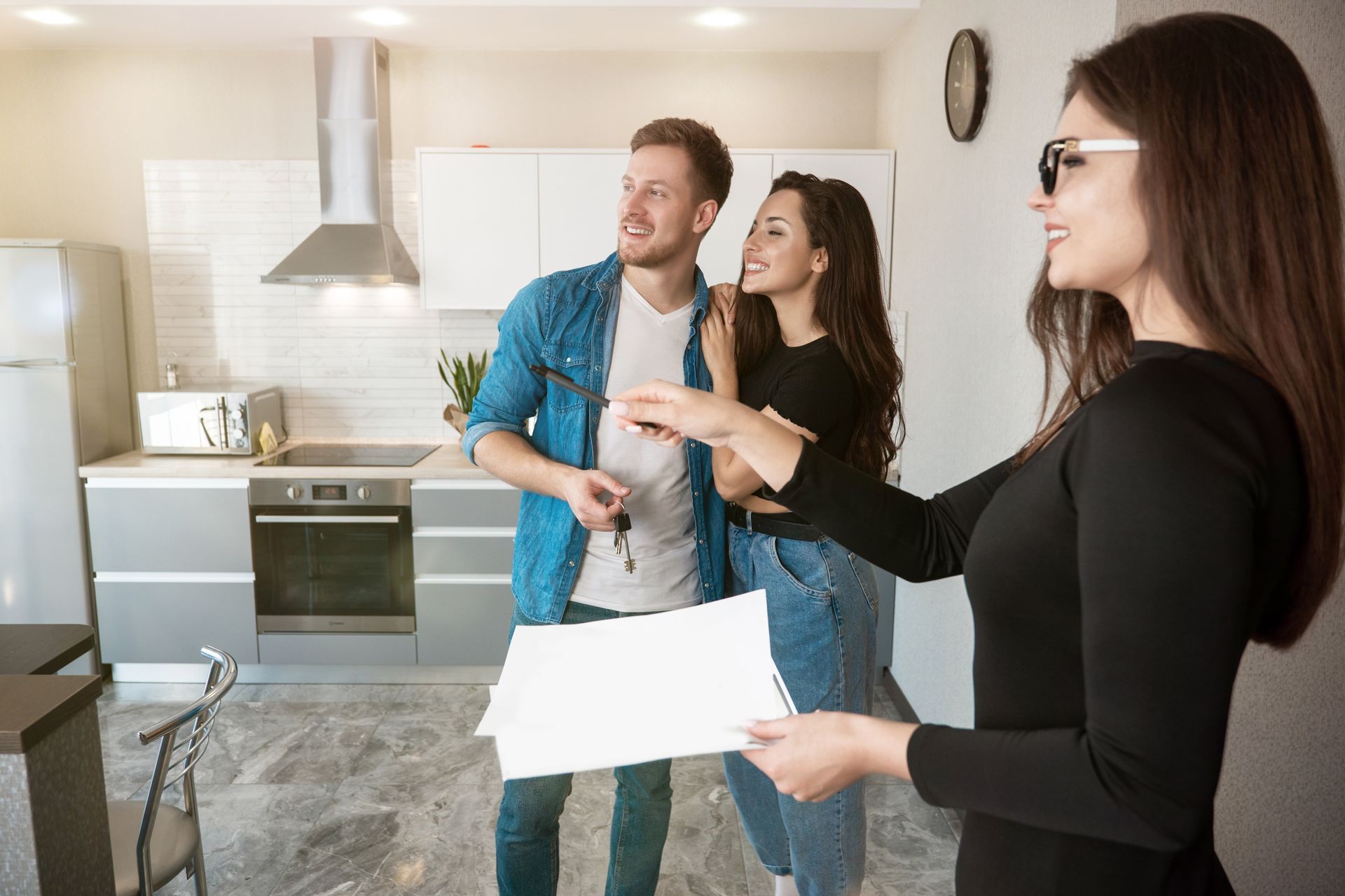 Real estate agent handing keys and paperwork to a couple in a modern kitchen.