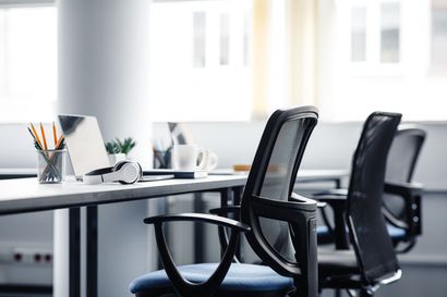 Office with desk, chairs, and laptop near window. Black mesh chairs and white desk.