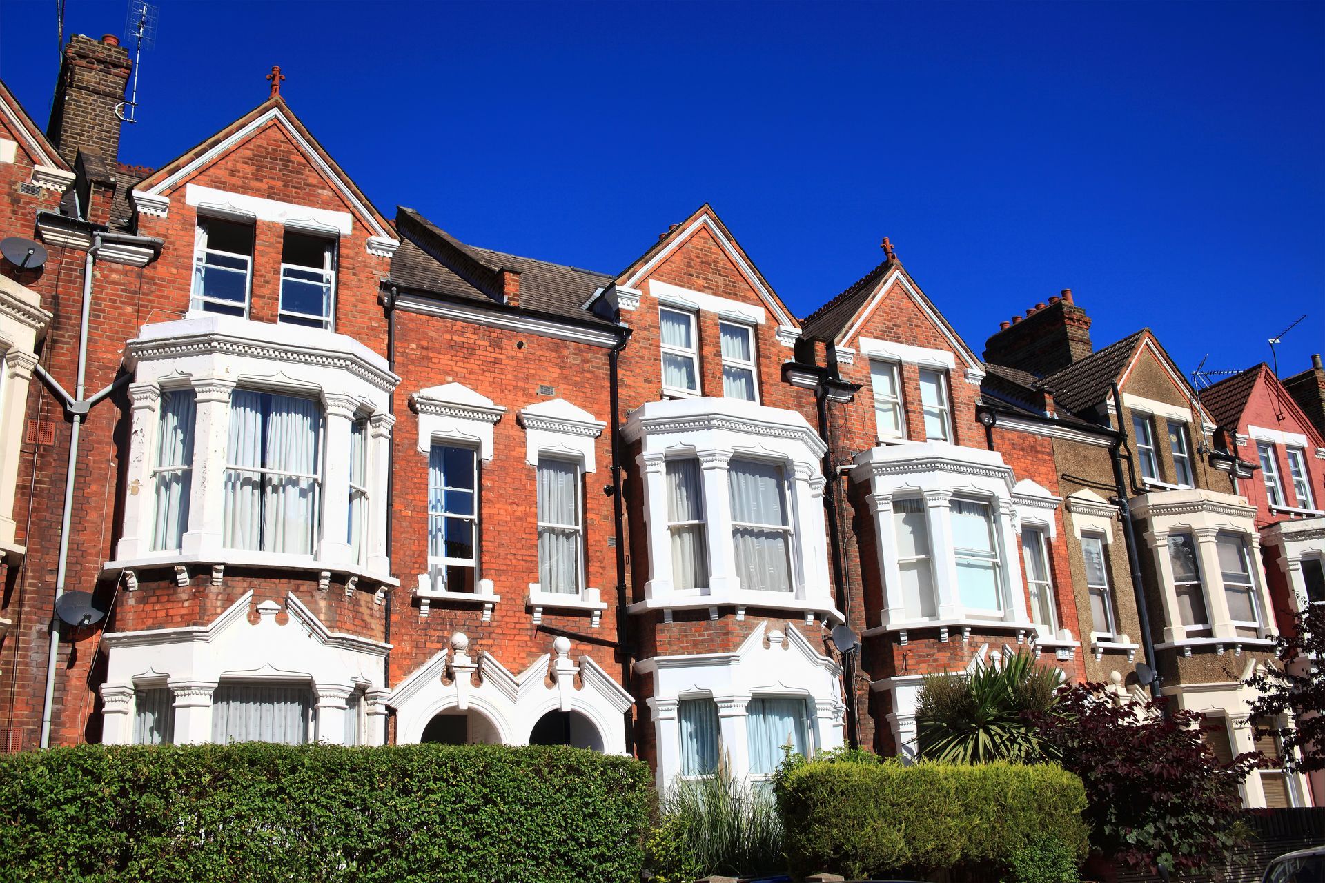 Row of red brick houses with bay windows under a clear, blue sky.