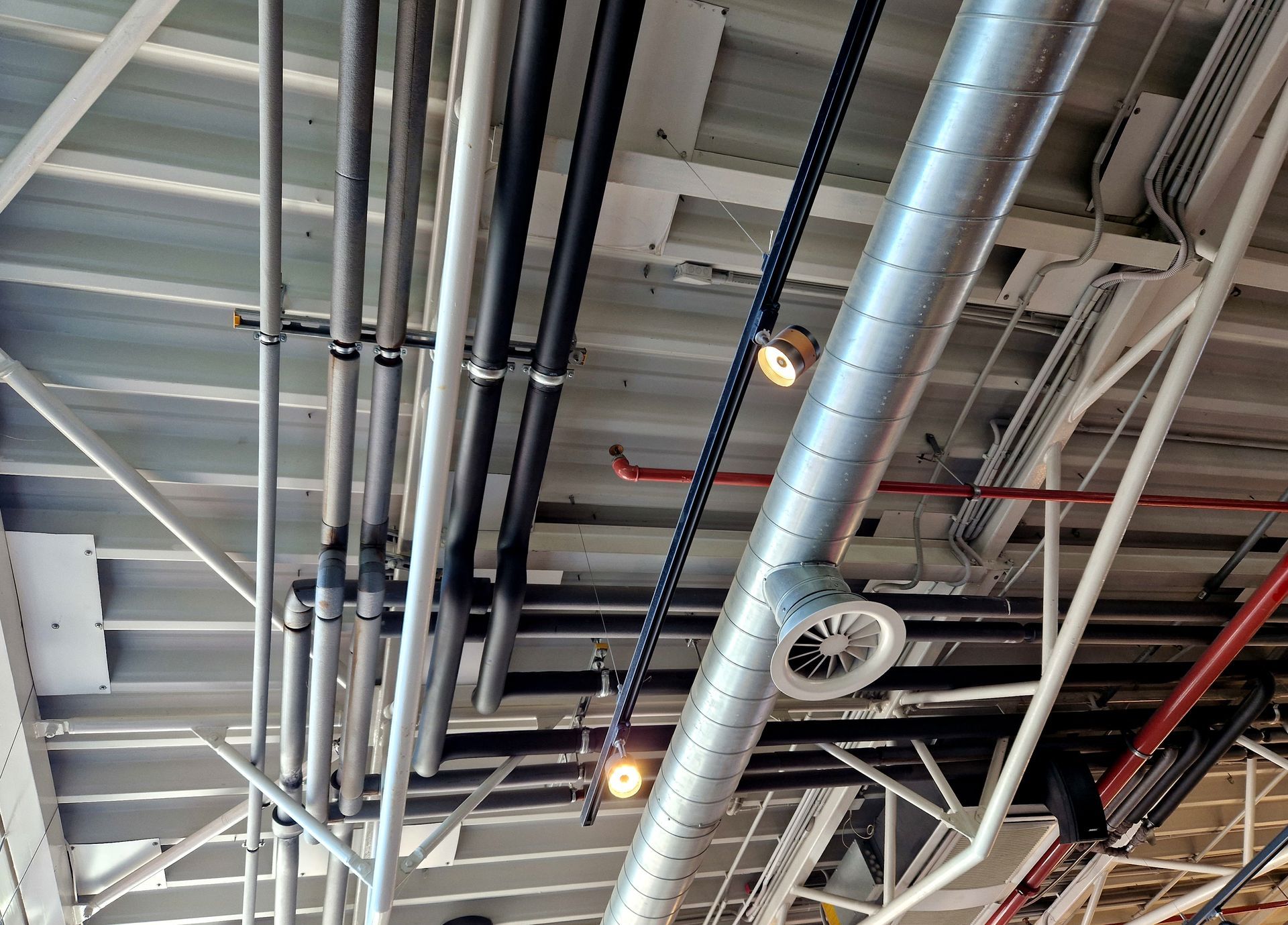 Pipes and ductwork on a white ceiling with exposed beams. Two small lights hang down.