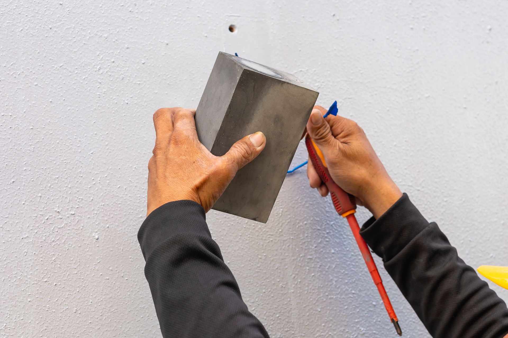 Person using a screwdriver and a block to install something on a white textured wall.