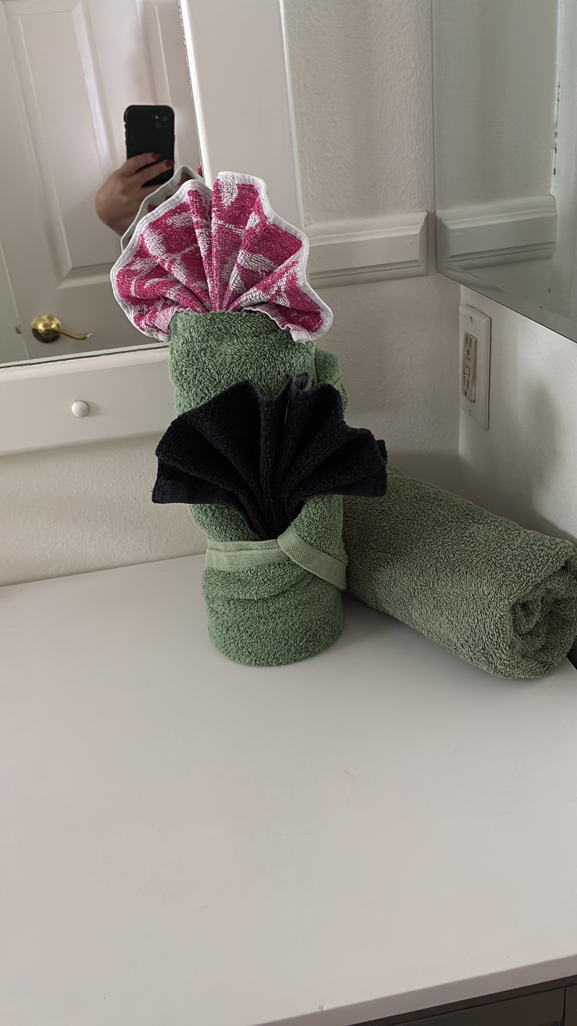 A person is taking a picture of a towel shaped like a flower in a bathroom.