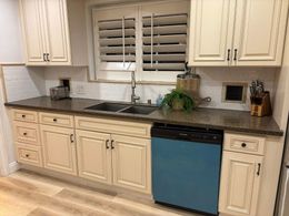 A kitchen with white cabinets , granite counter tops , a sink , and a blue dishwasher.