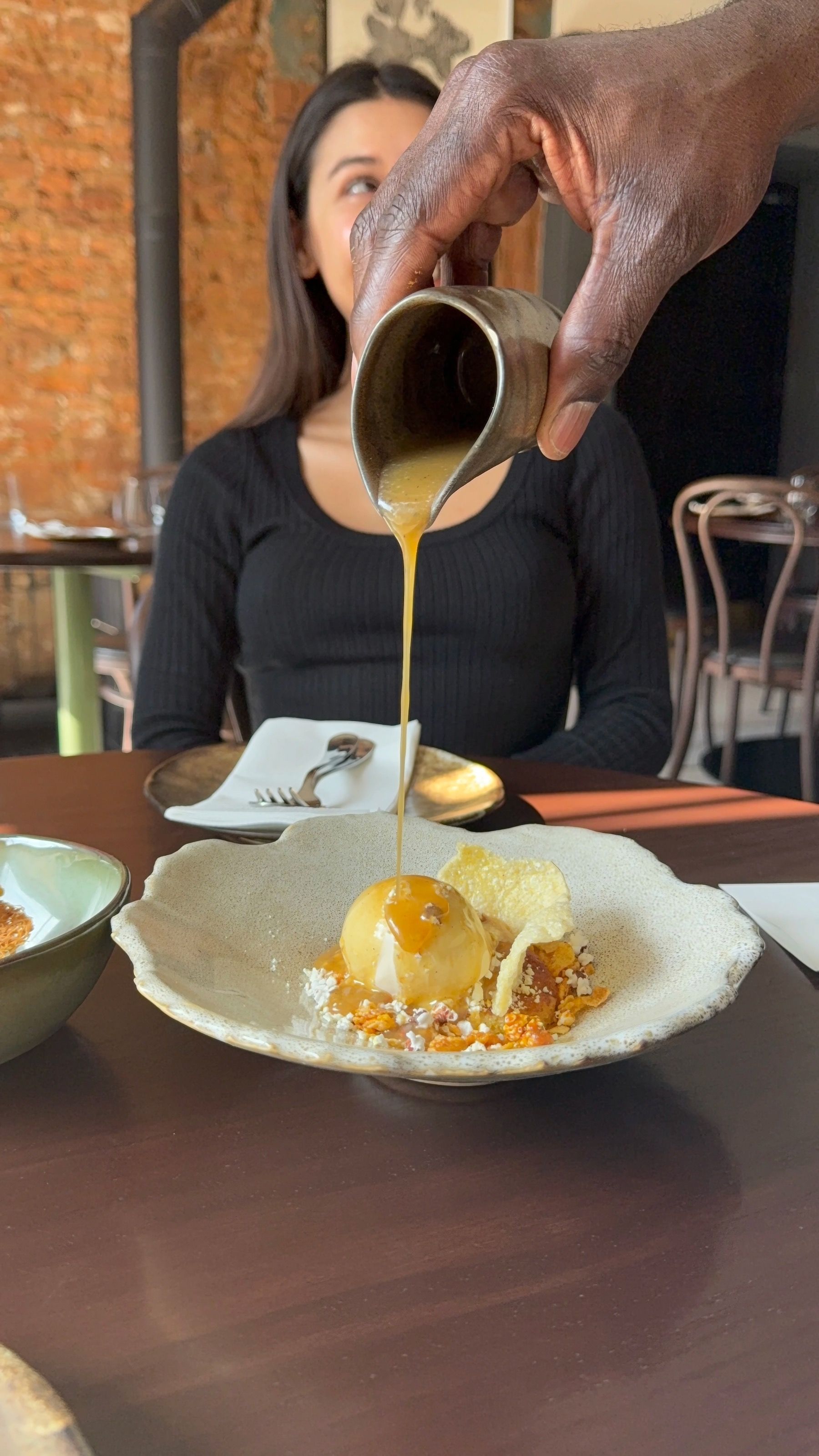 Server pouring dessert sauce at Chefs Warehouse & Canteen with Paige seated in background