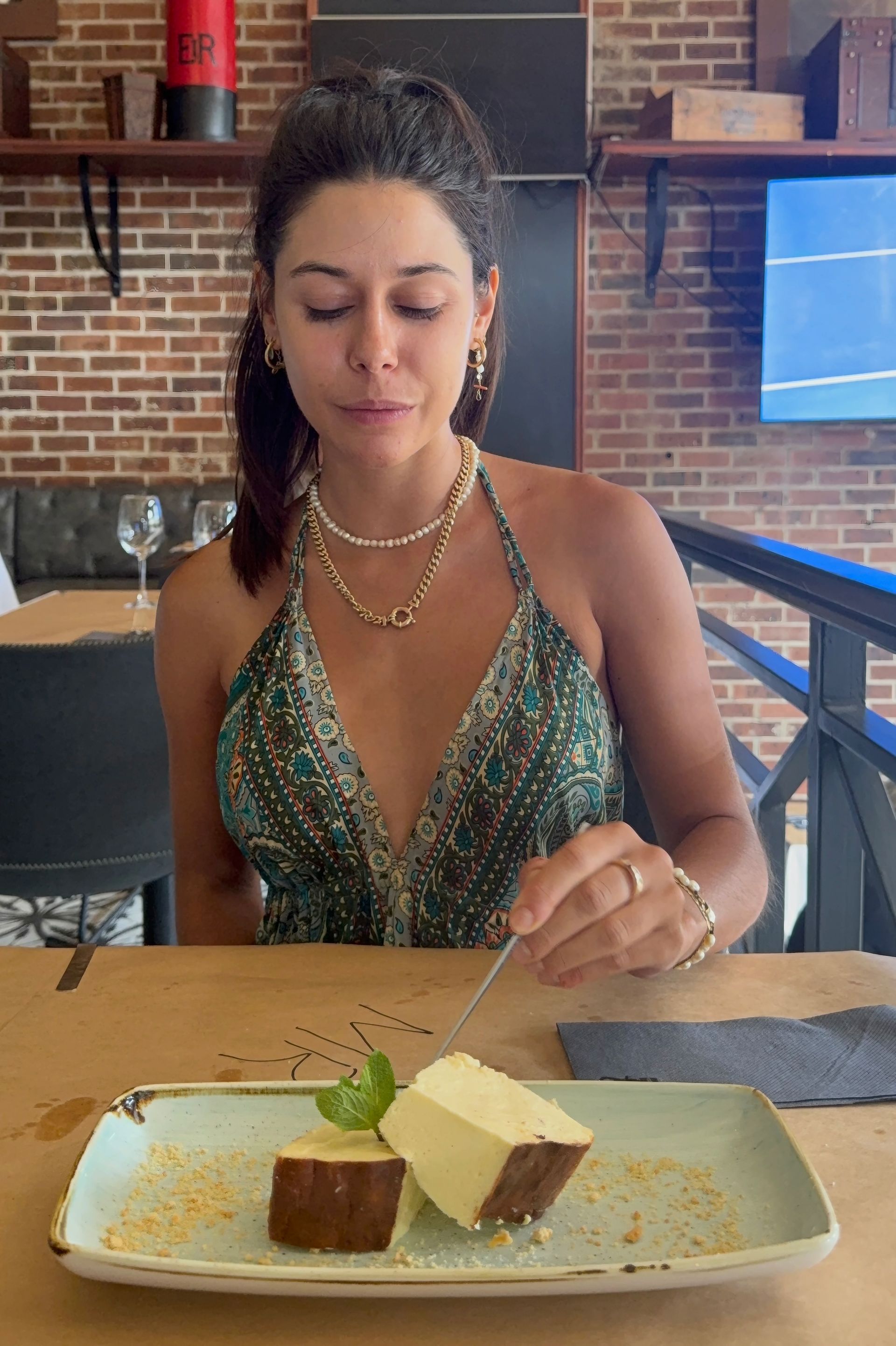 Woman at a restaurant, looking at cheesecake on a plate; holding a fork.