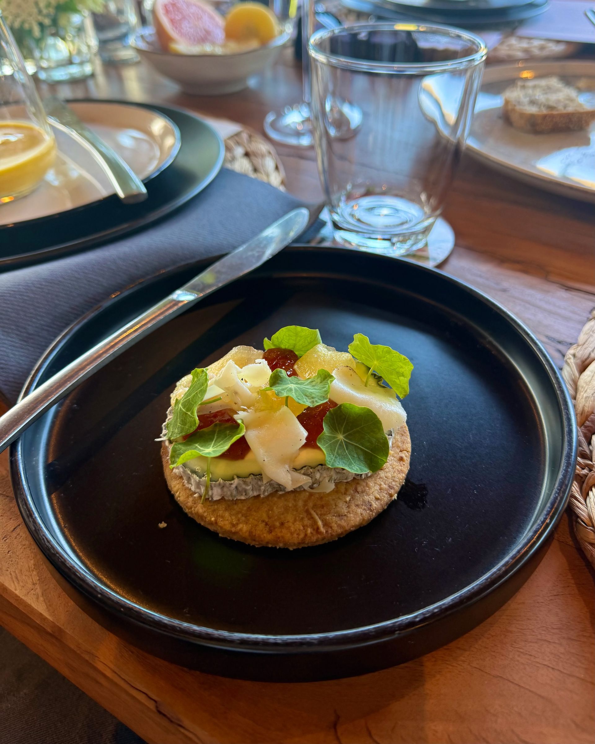 A small appetizer on a black plate with garnish. Knife and glass of water next to it.