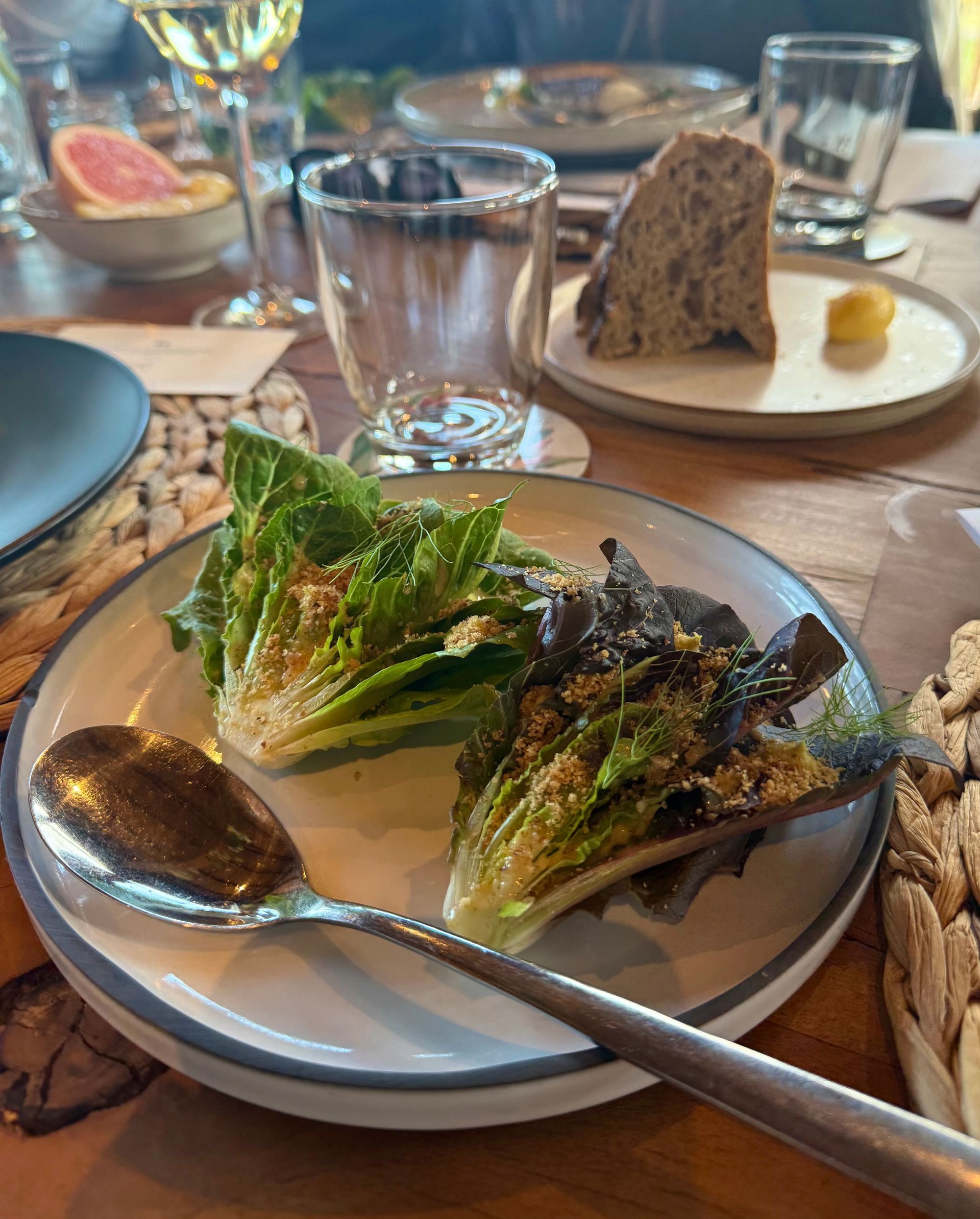 Romaine lettuce salad with dressing on a plate, alongside bread and drinks on a table.