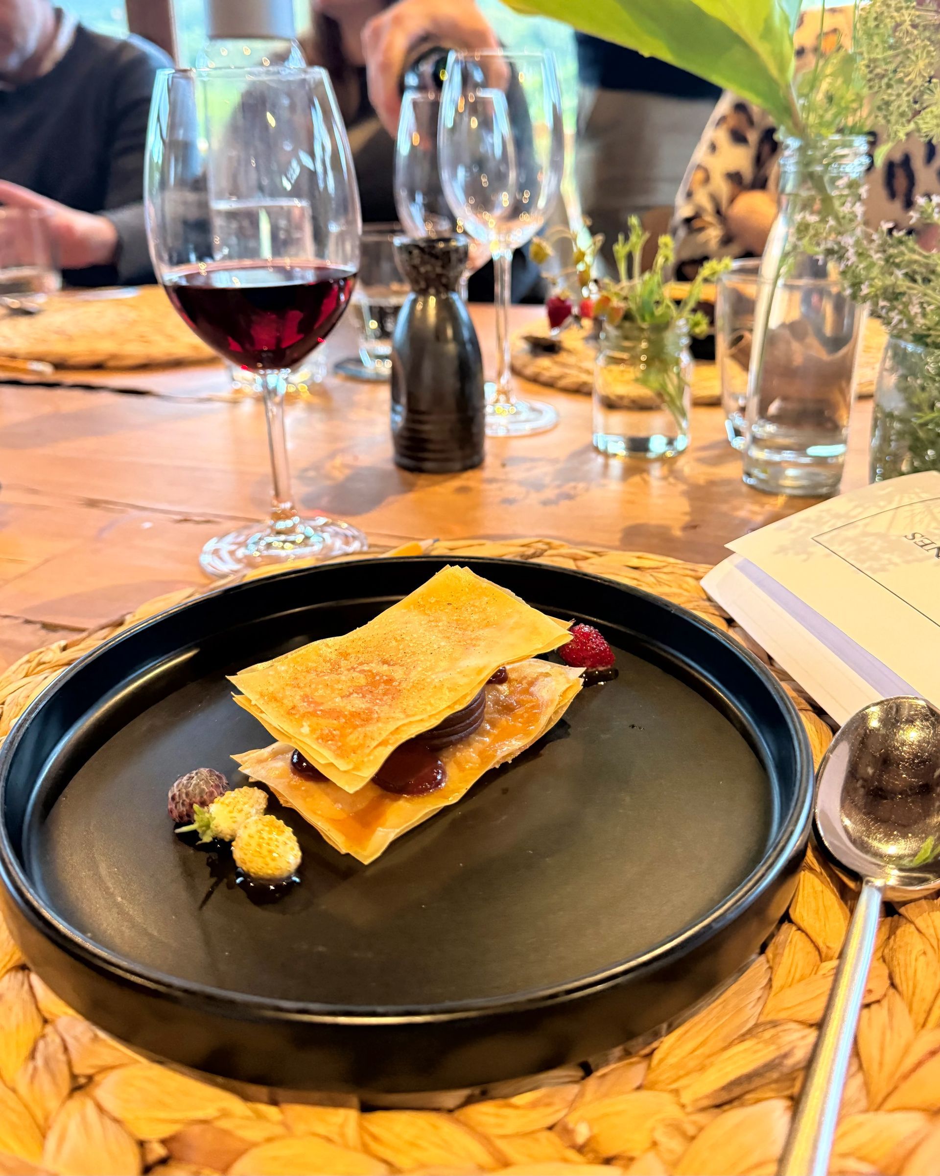 A small dessert on a black plate with red wine and a clear glass in a dining setting.