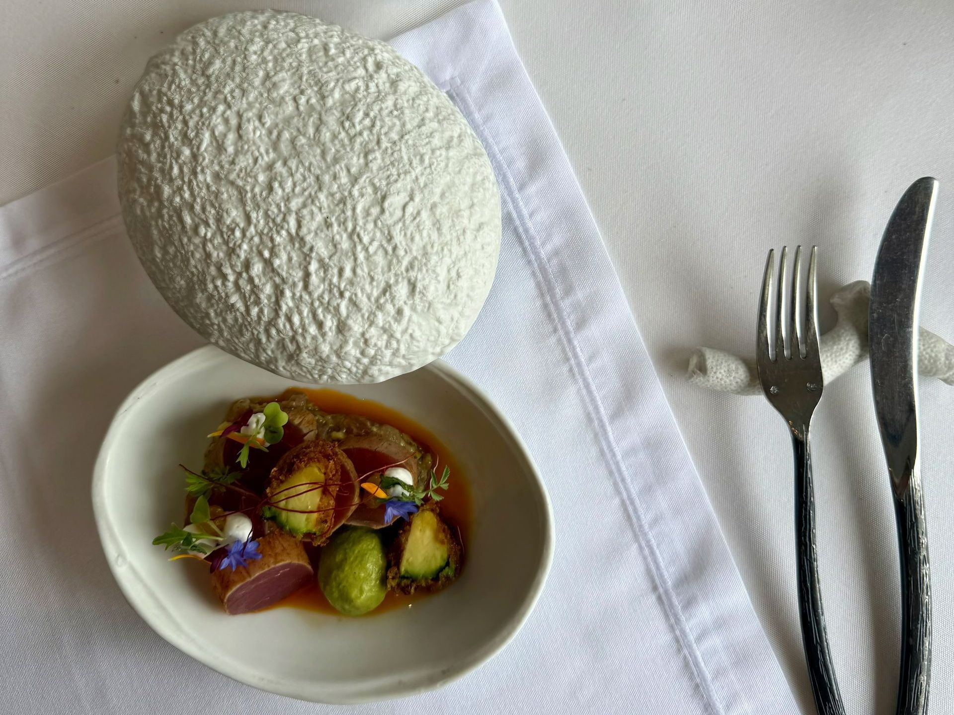 Plate of food with brussel sprouts, fork, knife, white napkin and decorative stone.