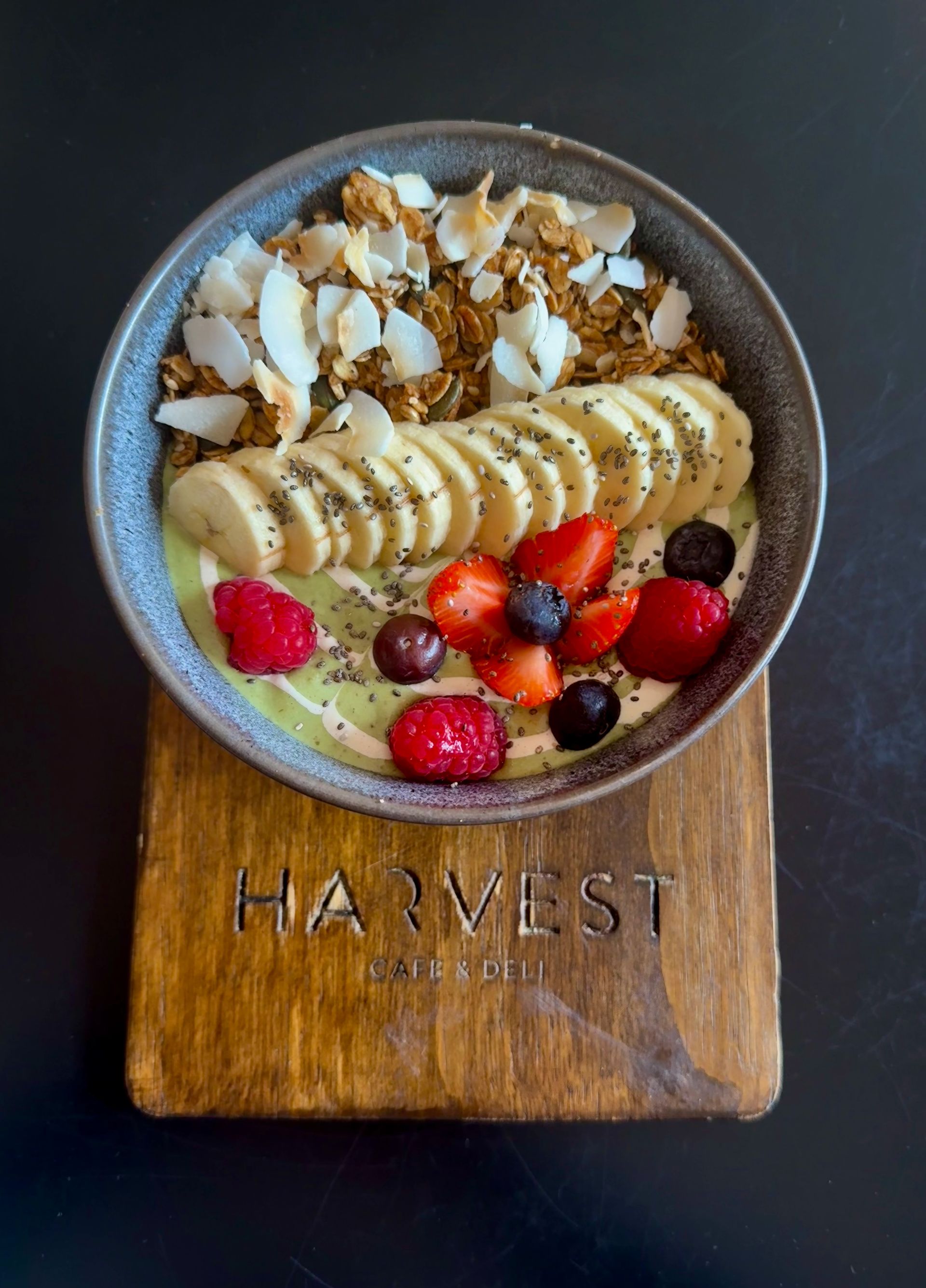 Acai bowl with granola, banana slices, berries, and coconut flakes on a wooden board.