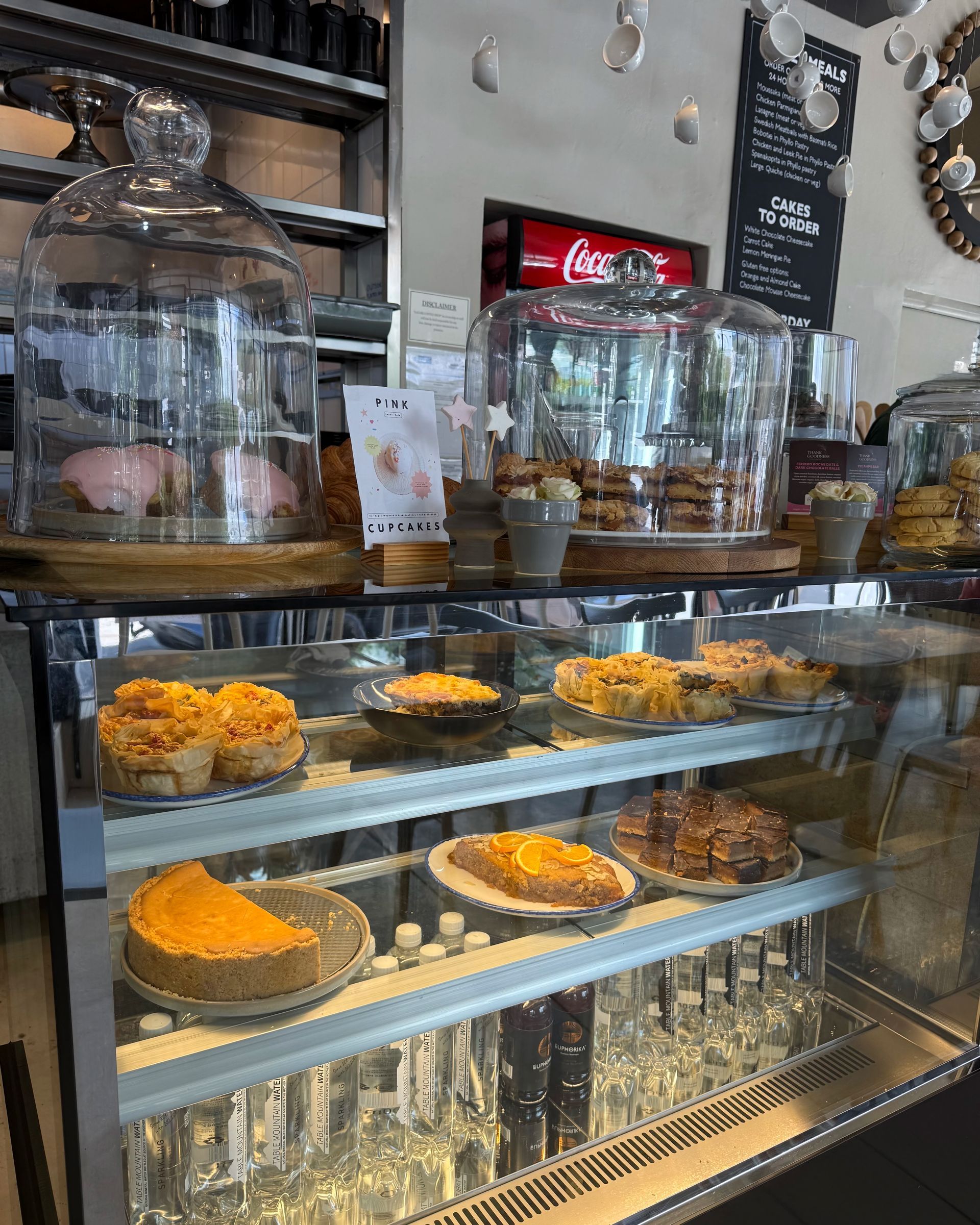 A glass display case in a cafe filled with pastries and cakes.  A Coca-Cola sign hangs in the background.