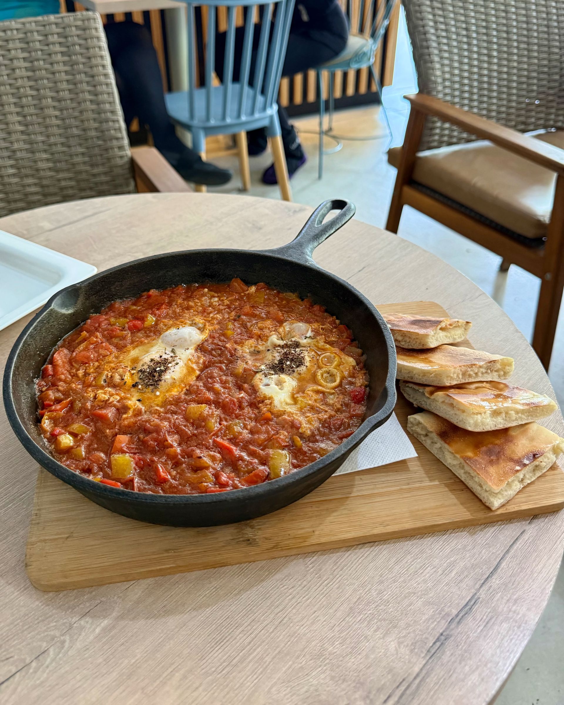 Skillet of shakshuka with bread, on a wooden board at a cafe table.