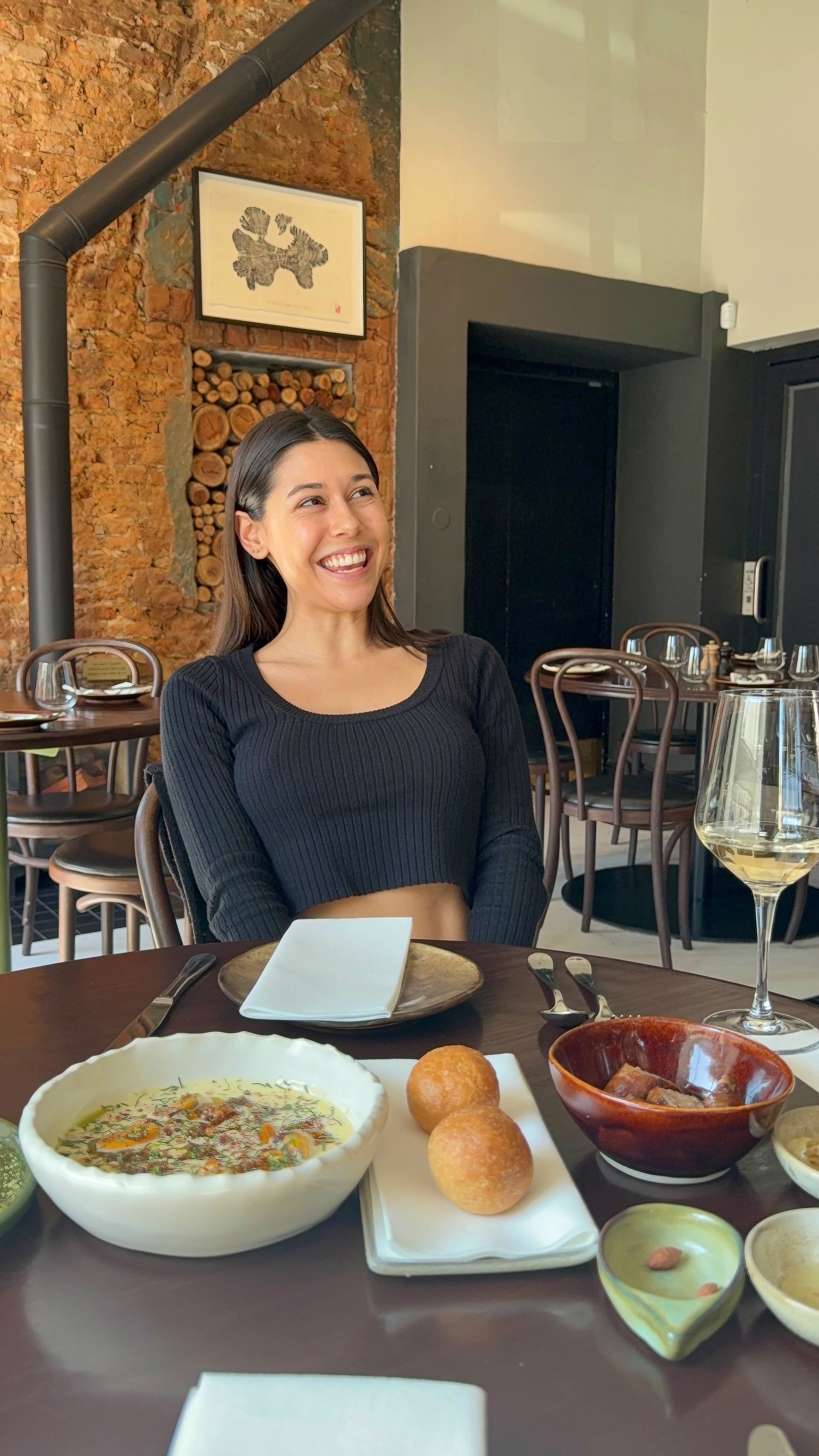 Woman laughing at a restaurant table with food and drinks.
