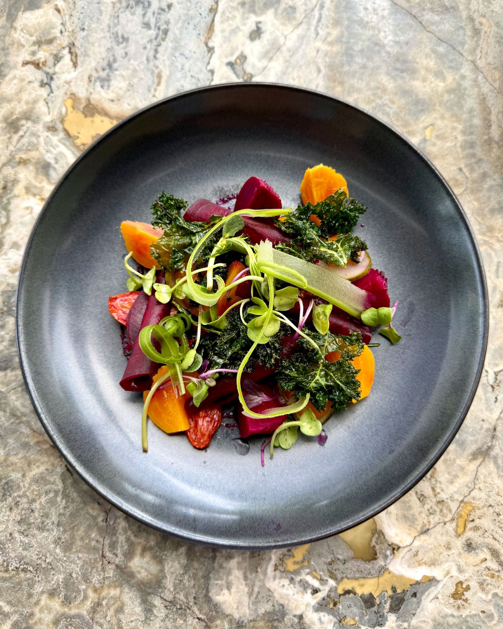 Beet salad with orange slices, kale, and microgreens on a gray plate.