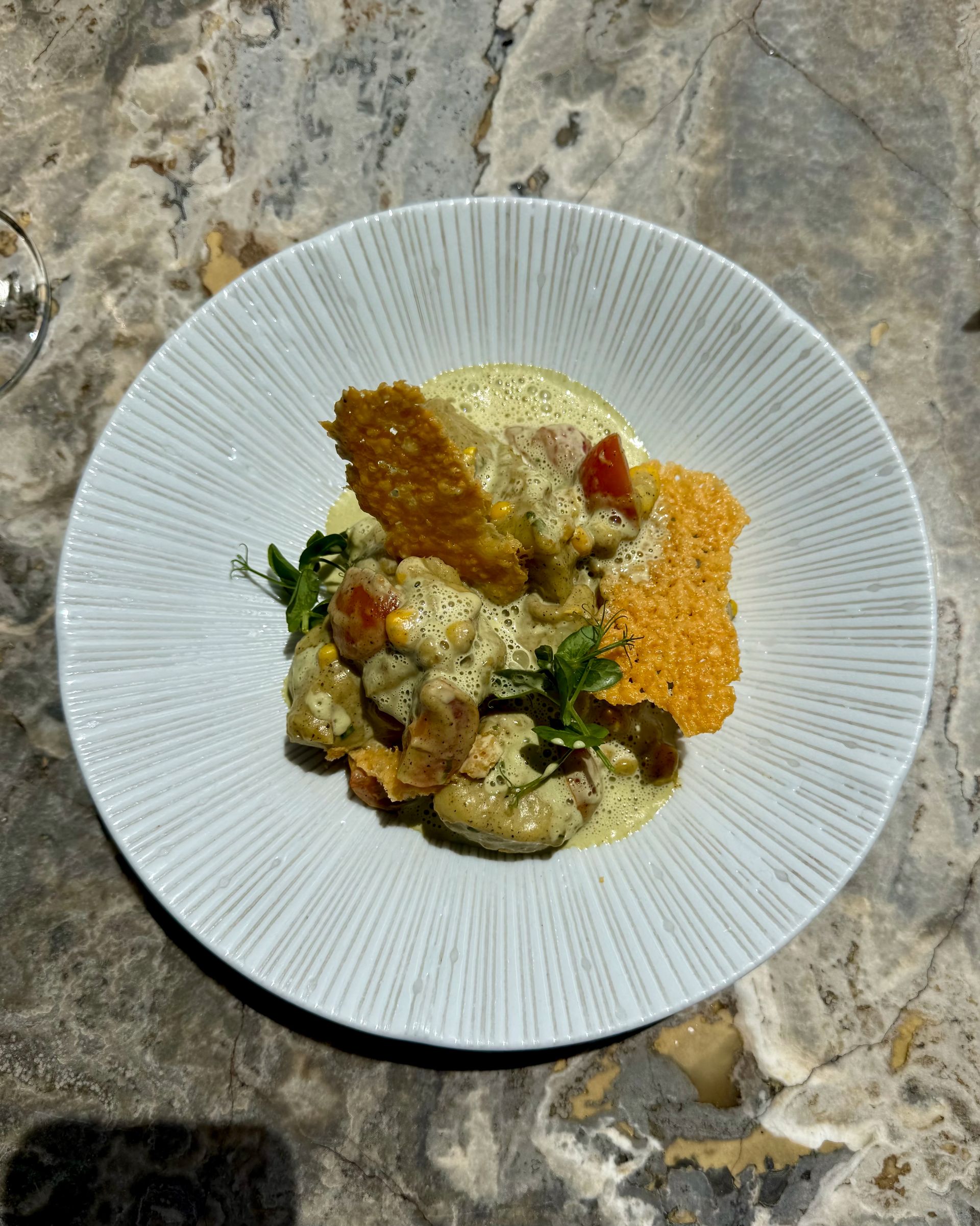 A plate of food with creamy sauce, tomatoes, and crispy cheese crackers, on a marble table.