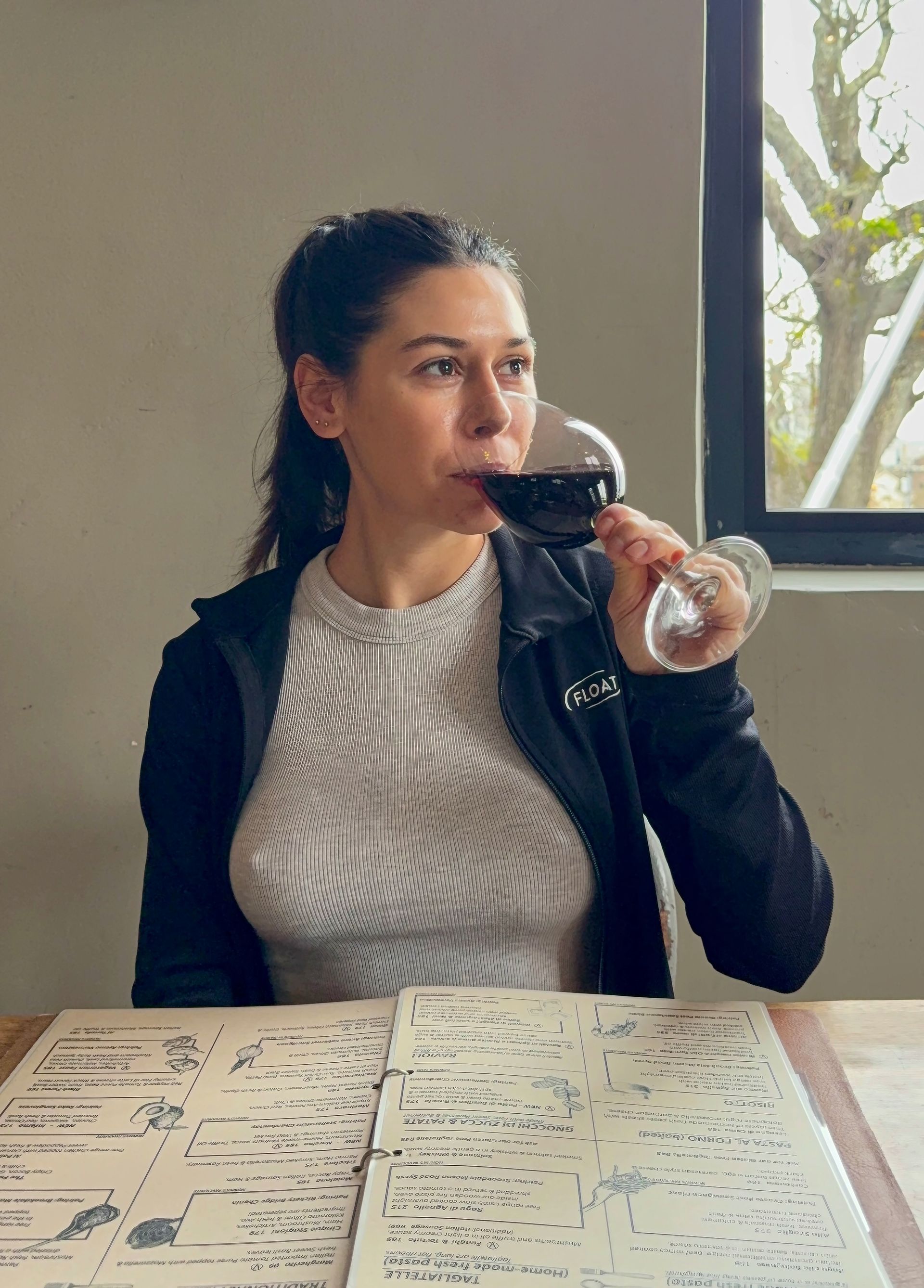 A wine glass with golden liquid on a wooden table by a window overlooking a patio.