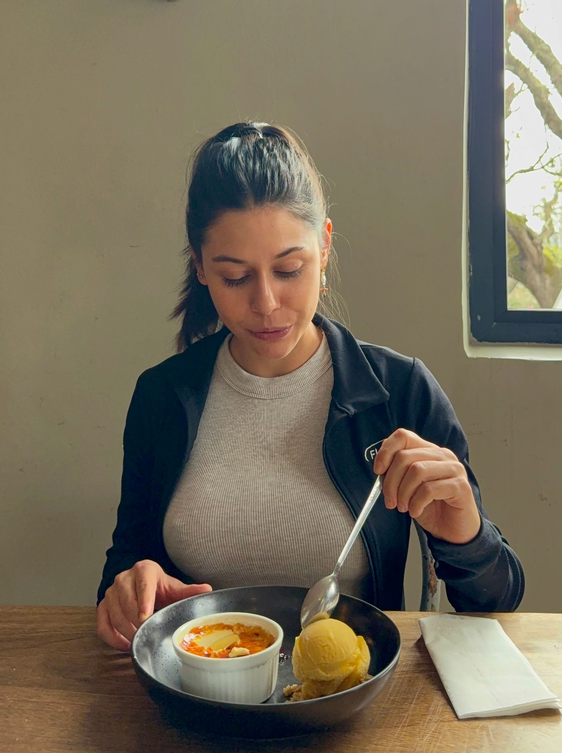 Chef pouring sauce over dessert; woman watches at a restaurant table.