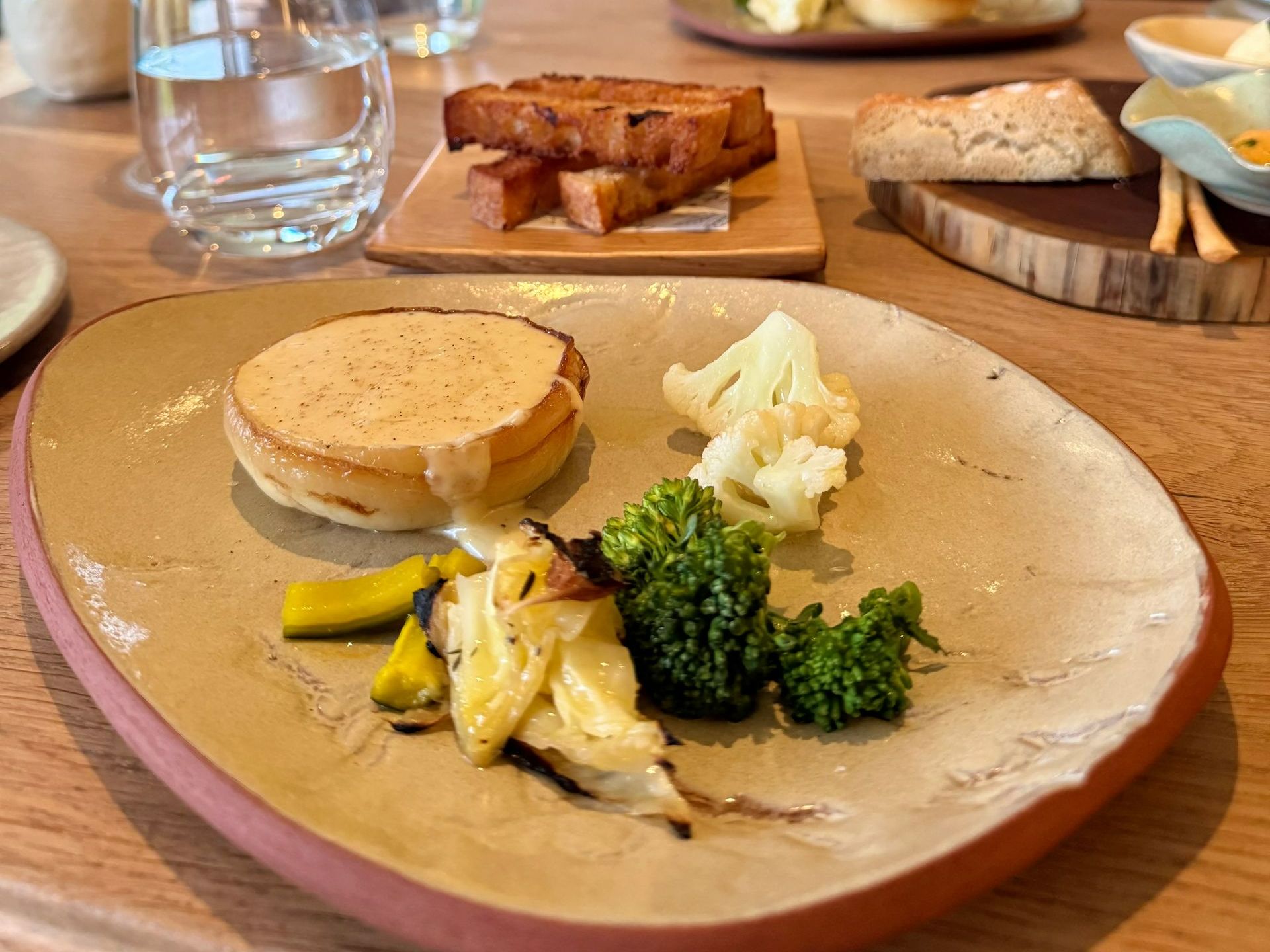 Plate of food: roasted vegetables, round bread topped with sauce, and other bread items.