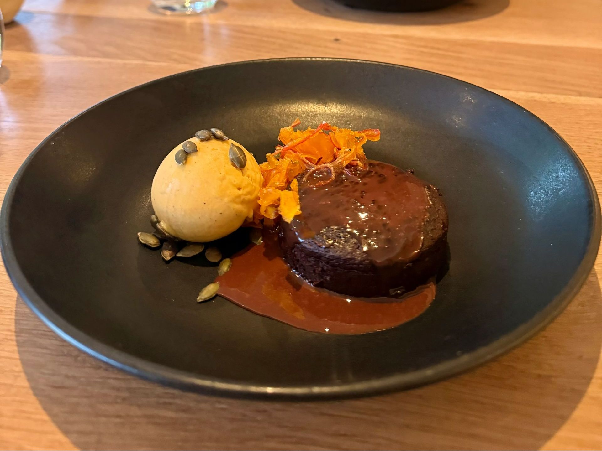 Chocolate cake with pumpkin ice cream and garnish on black plate.