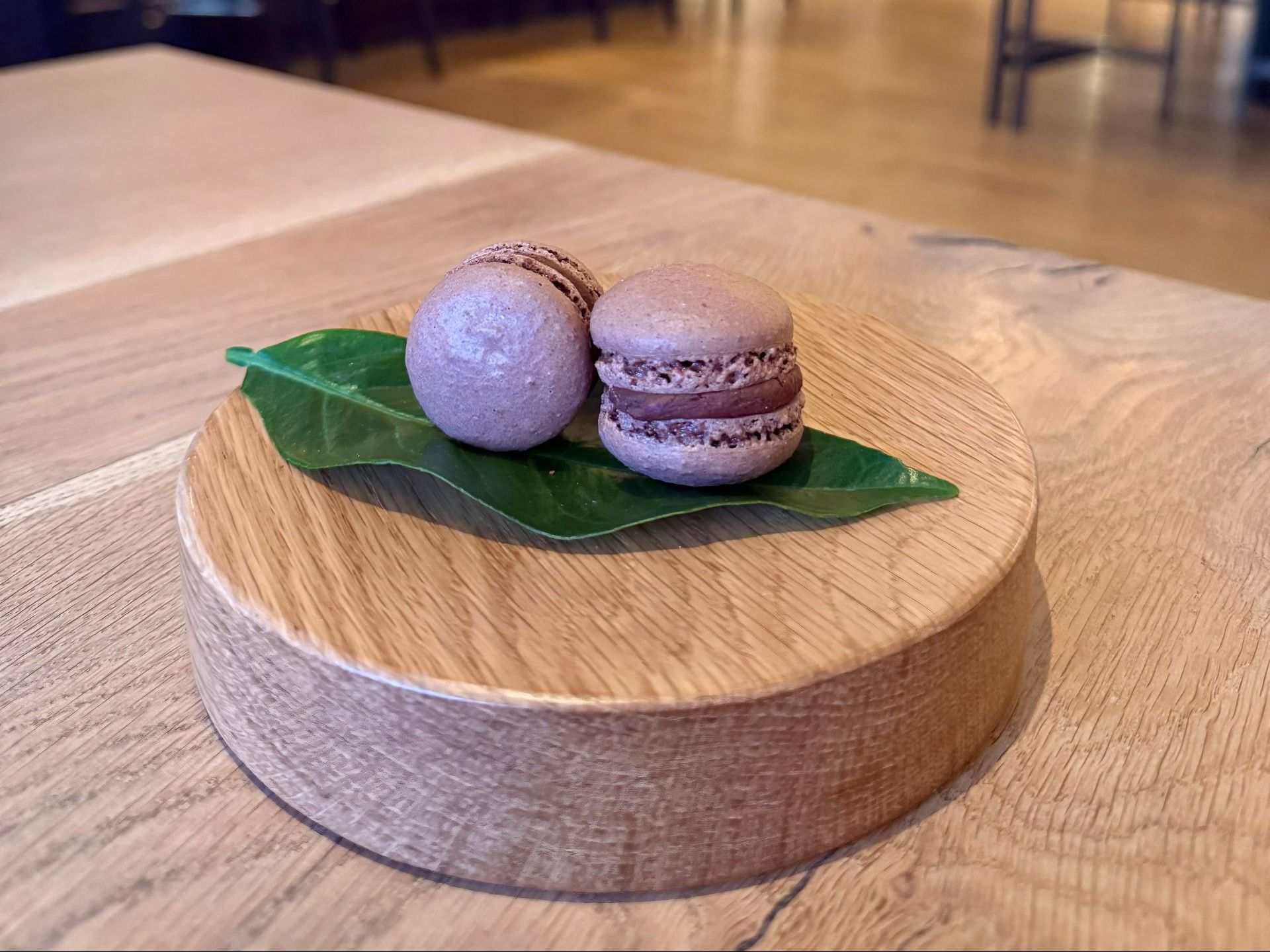 Two purple macarons on a wooden stand with a green leaf, on a wooden table.