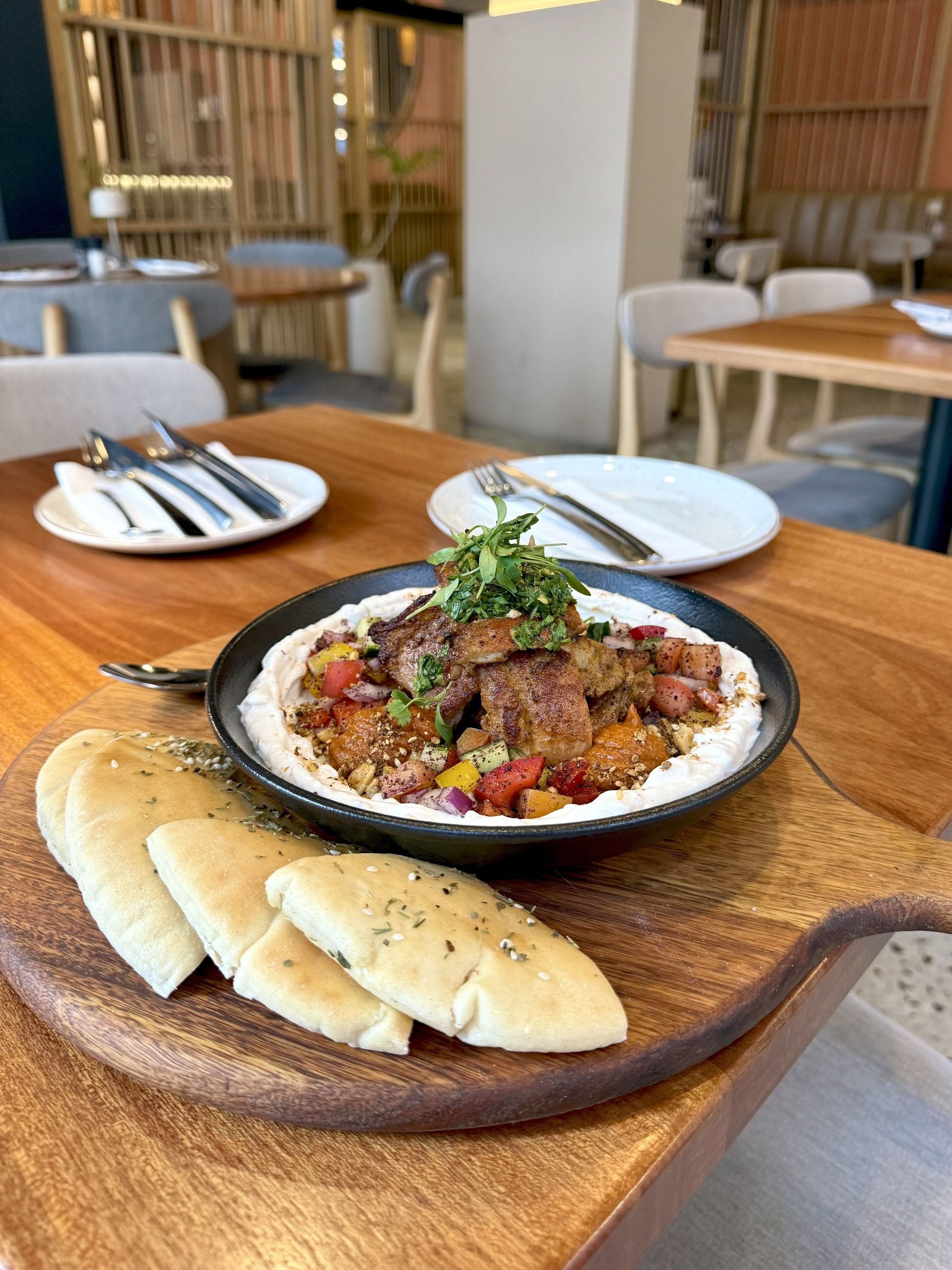 Dish of meat with vegetables on hummus, pita bread, on a wooden board in a restaurant.
