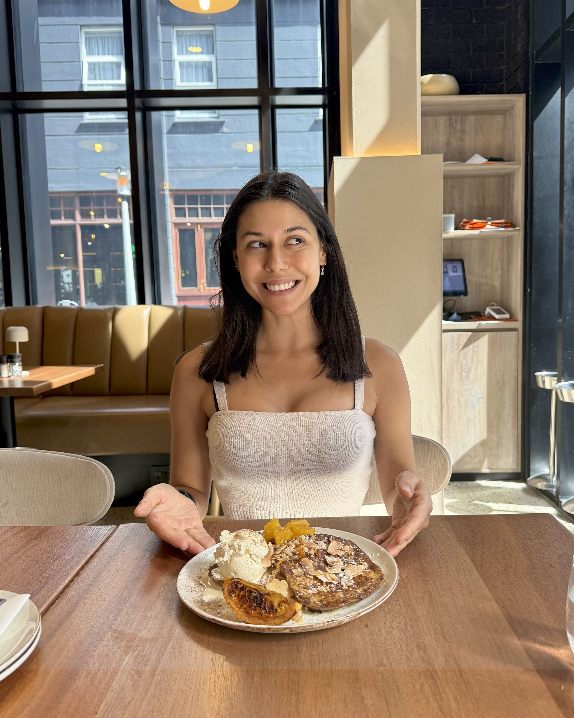 Woman smiles excitedly at a plate of pancakes in a bright cafe.