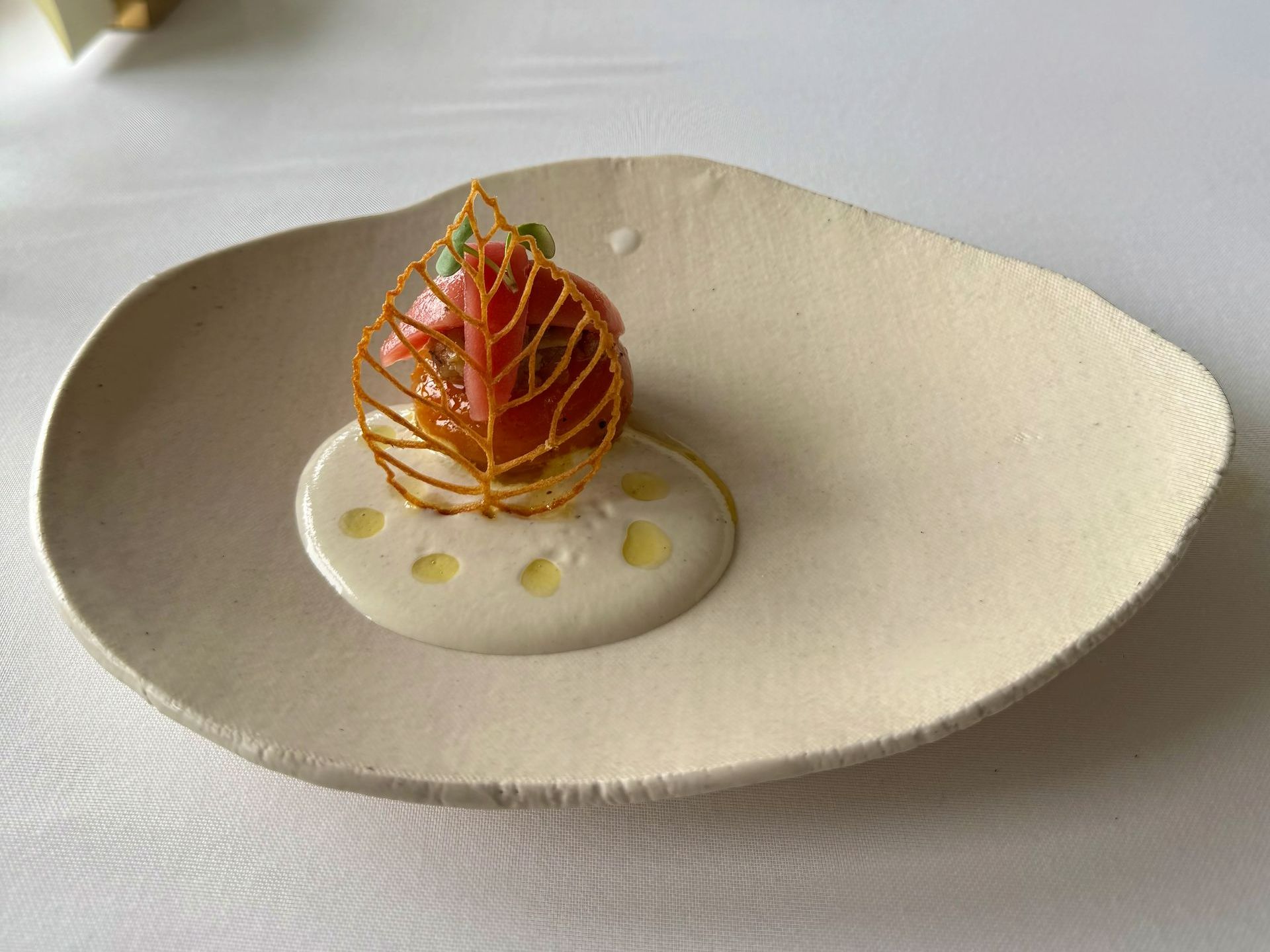 Elegant dish: Tomato wrapped in a gold lattice, served on a white sauce-covered plate.