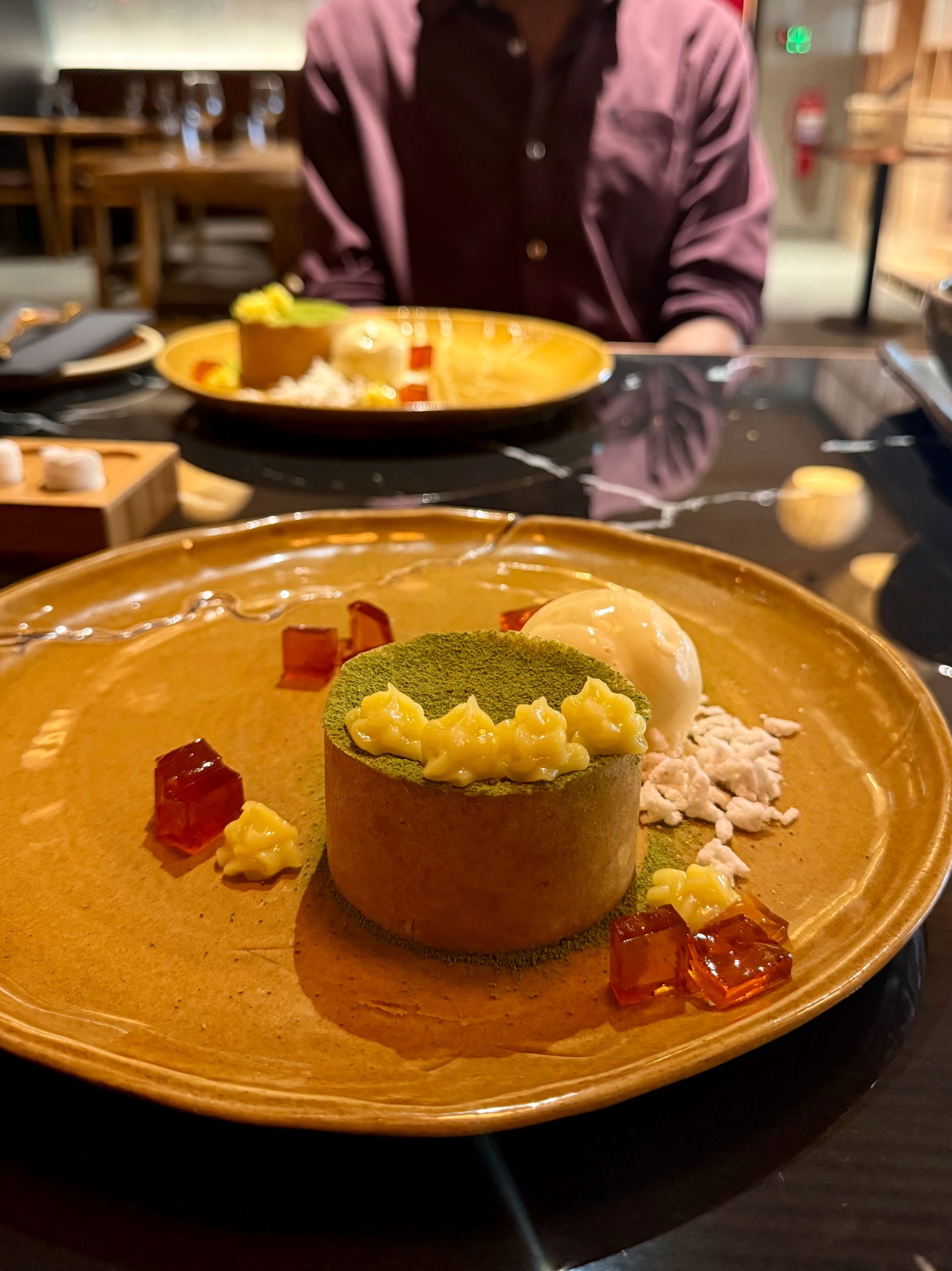 Dessert on a gold plate: a green-topped pastry with cream and jelly, served in a restaurant.