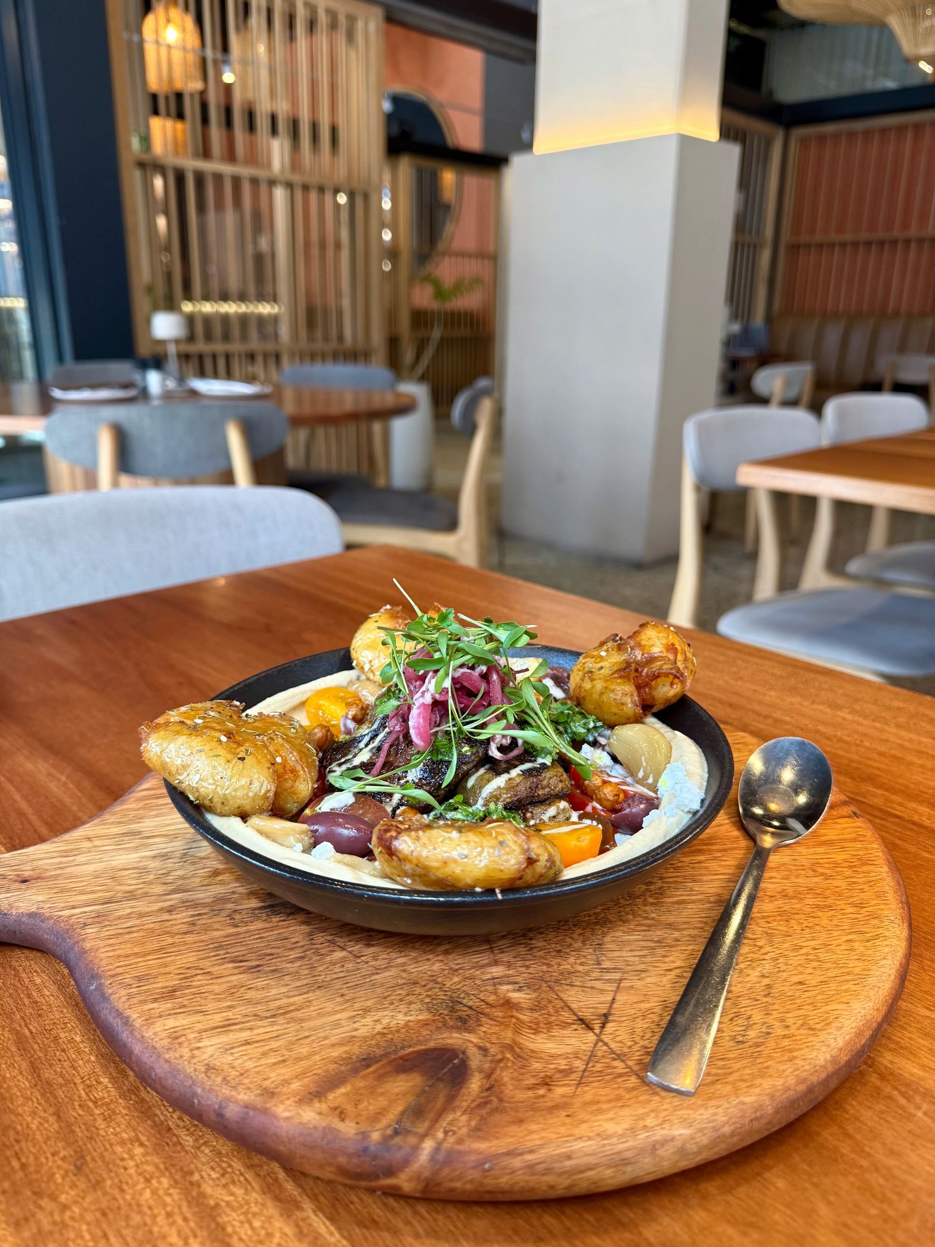 Dish of food with potatoes, vegetables, and sprouts, served on a wooden board in a restaurant.