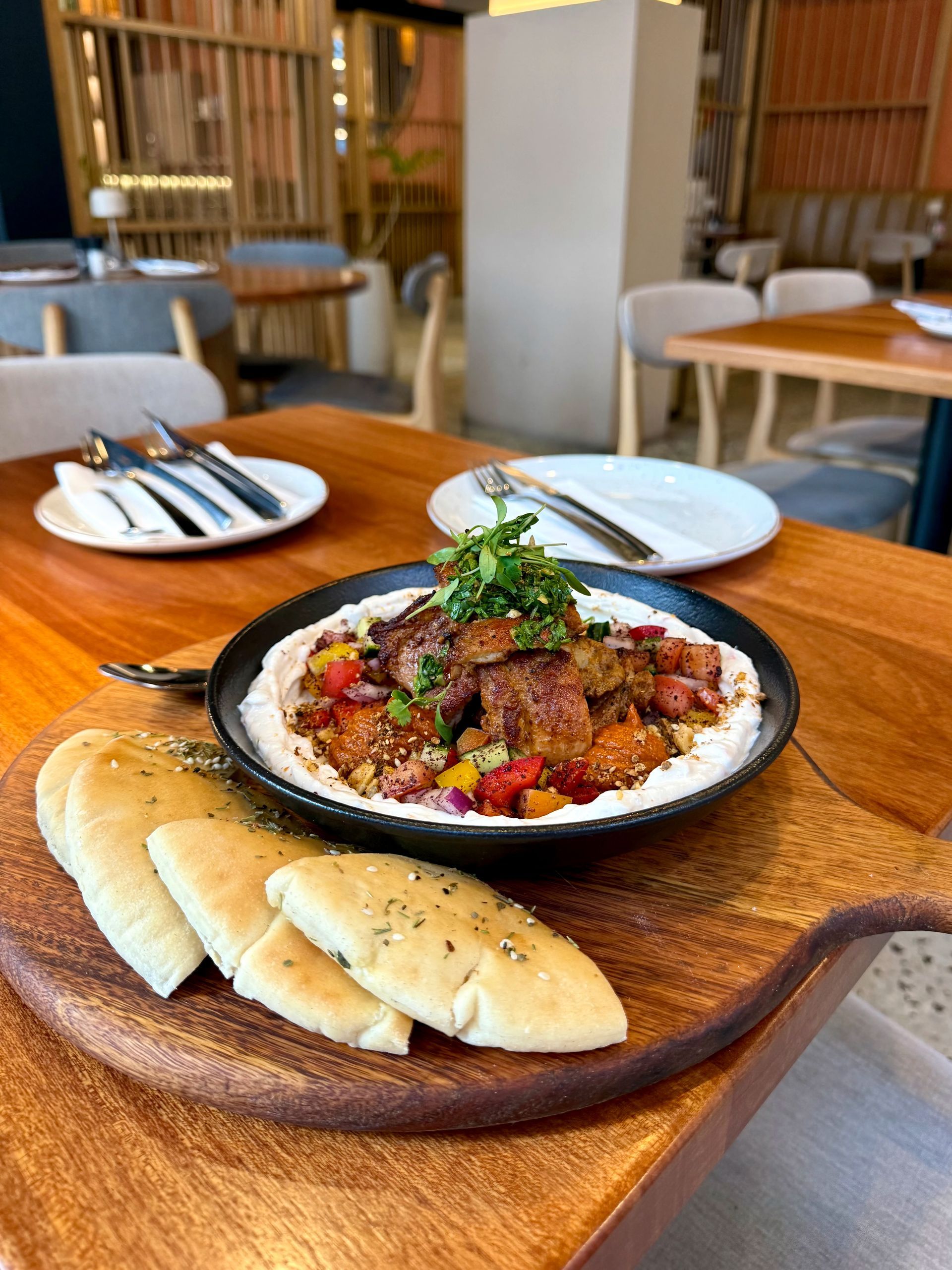 Dish of cooked meat with pita bread on wooden table in restaurant.