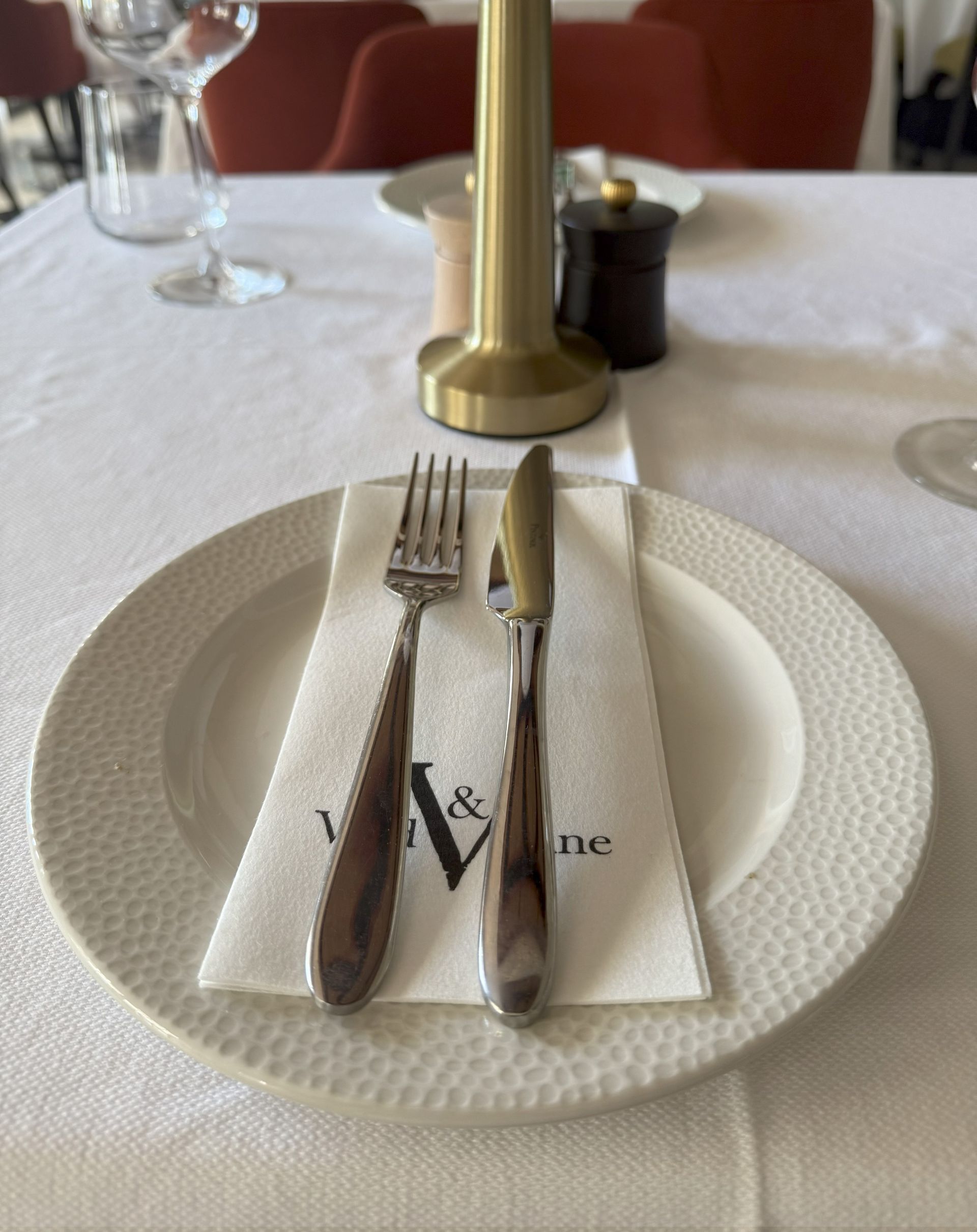 Table setting: white plate, fork, knife, napkin with "V&V" logo.