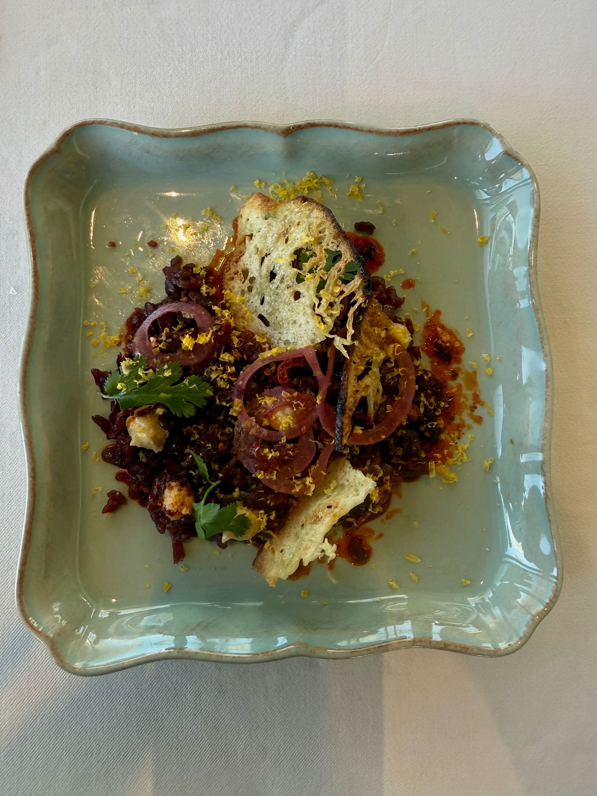 Gourmet salad on a light green plate. Features red onions, croutons, and a crumbly, dark base.