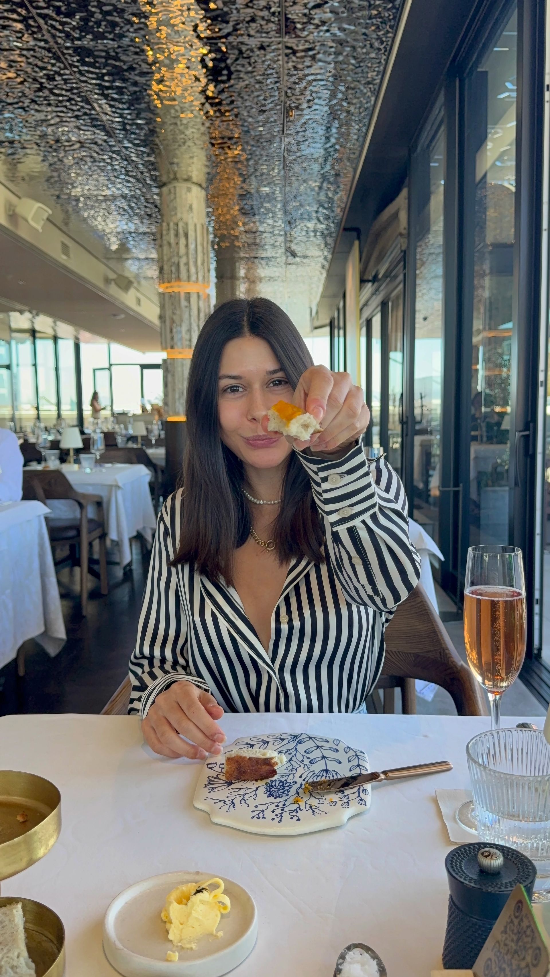 Woman in striped shirt at fancy restaurant, holding food, looking at camera.