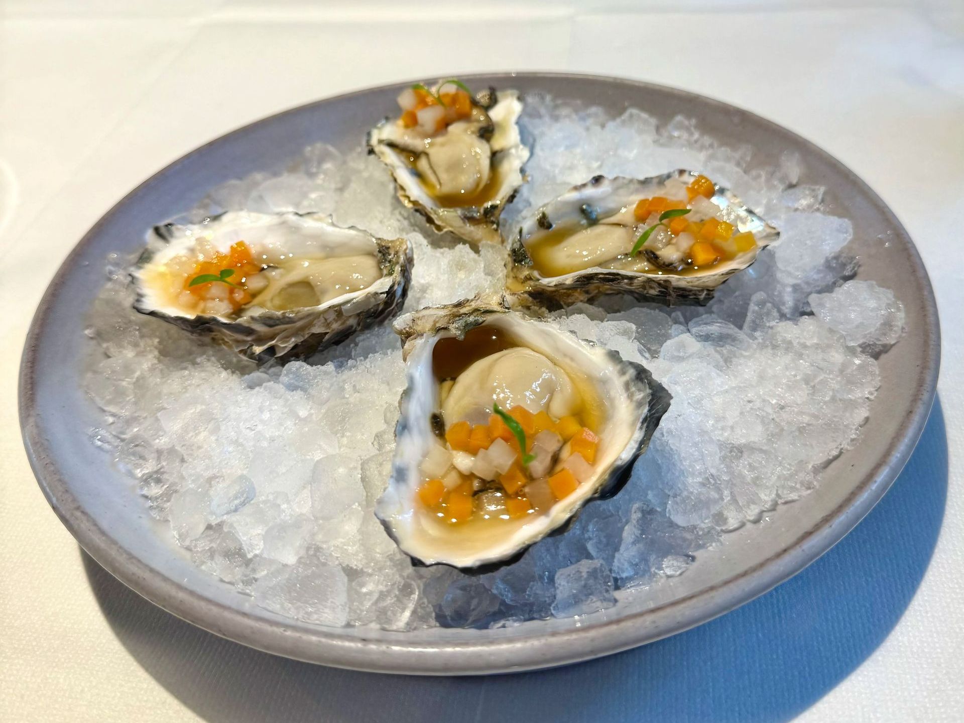 Four oysters on a plate of ice, topped with orange and green garnish.