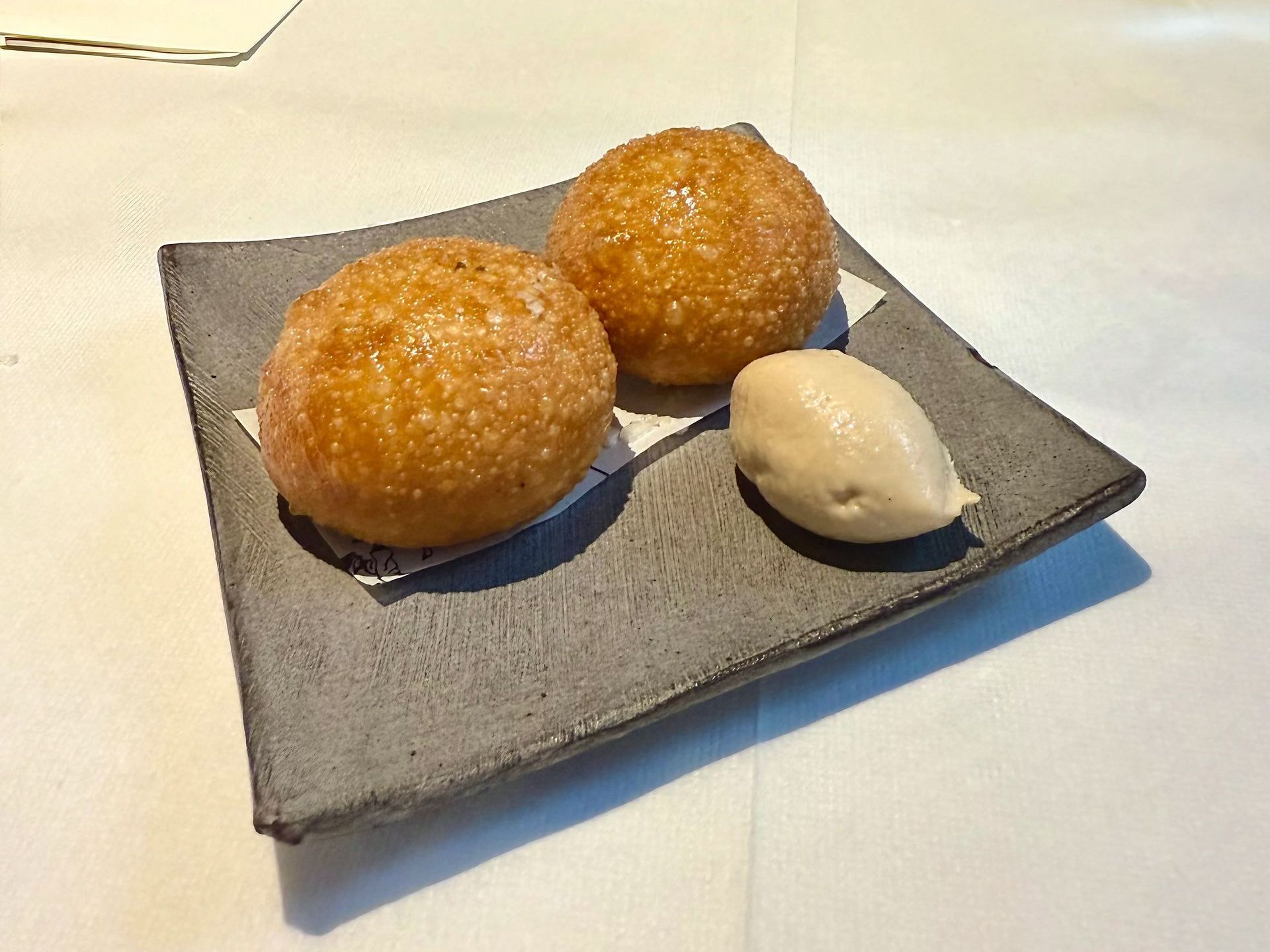 Two fried dough balls and a scoop of ice cream on a gray square plate, on a white tablecloth.