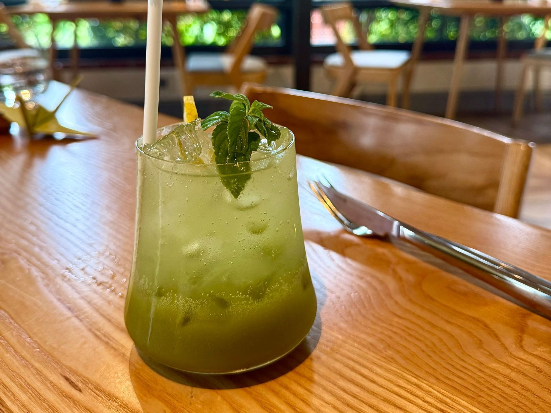 Green cocktail in a glass with ice, mint, and a straw, on a wooden table.
