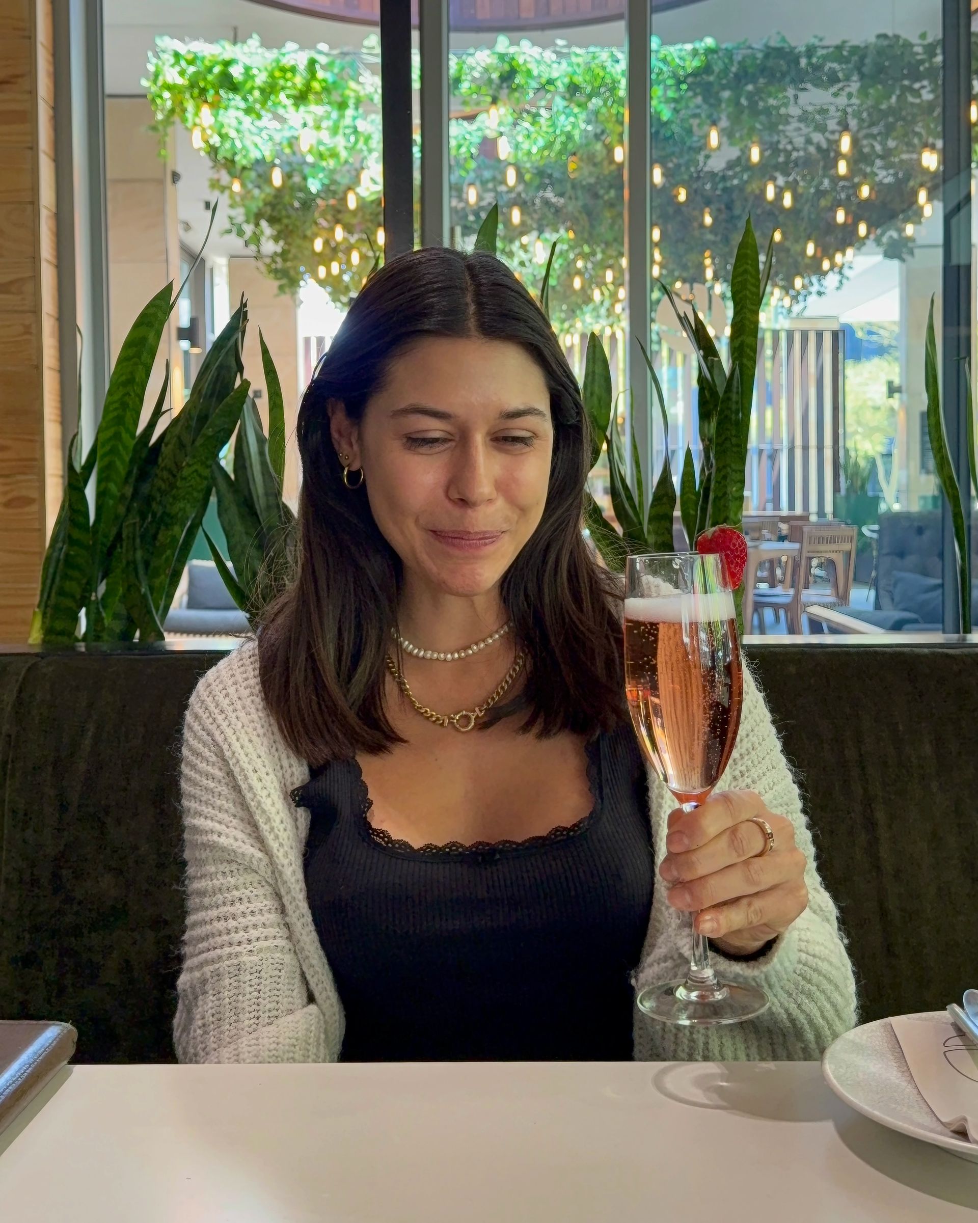 Woman holding champagne, winking at the camera, at a restaurant.