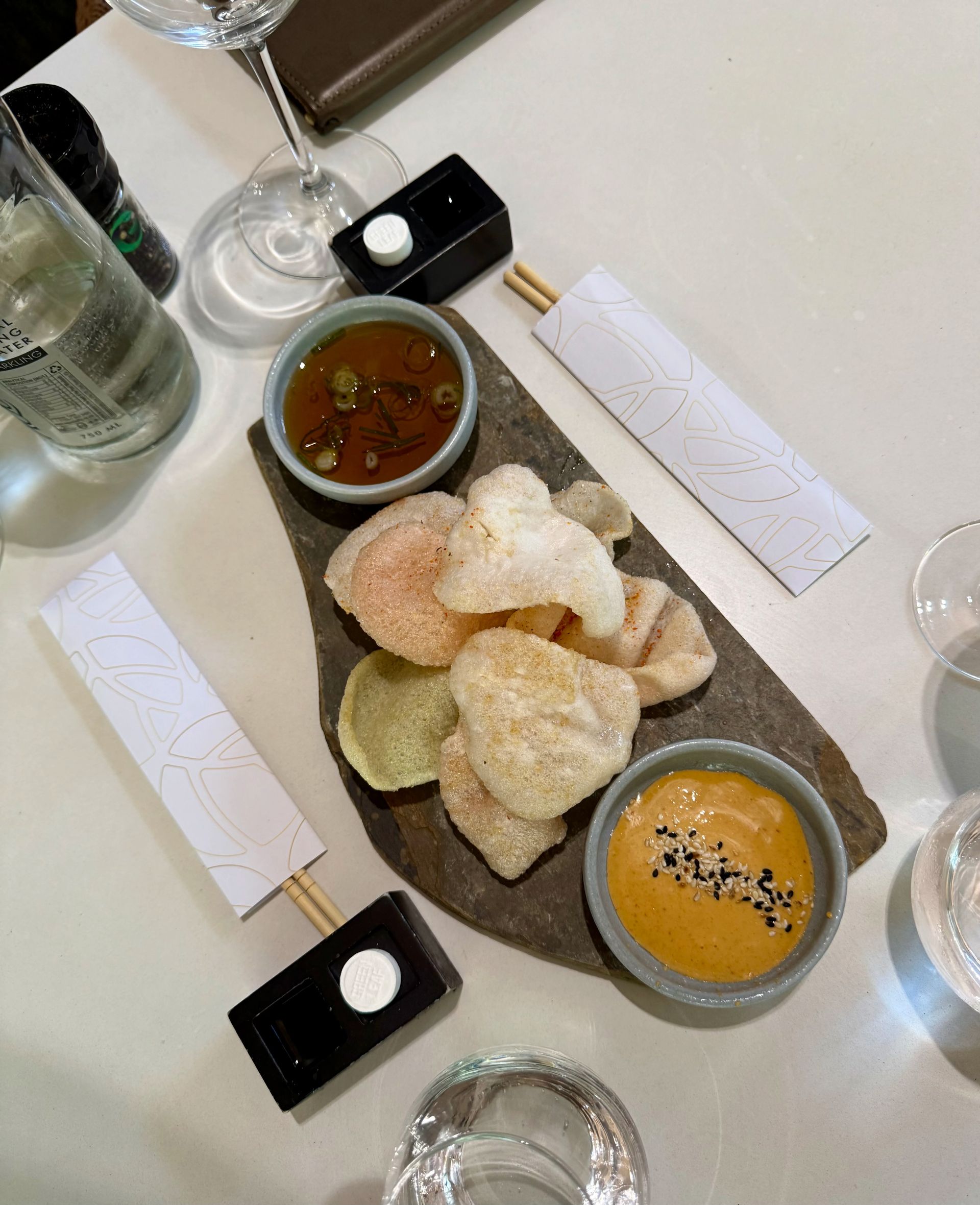 Chips with dipping sauces on a stone serving board, with chopsticks and glasses on a white table.