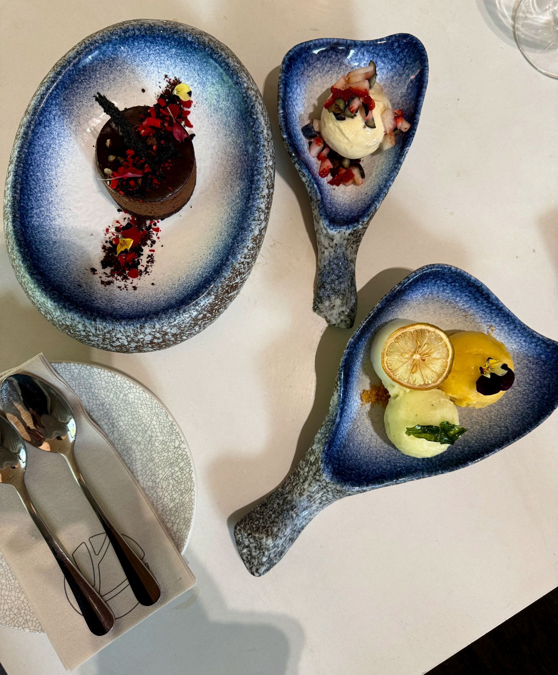 Desserts on blue and white patterned plates. Includes chocolate cake, ice cream, and lemon desserts, with spoons.