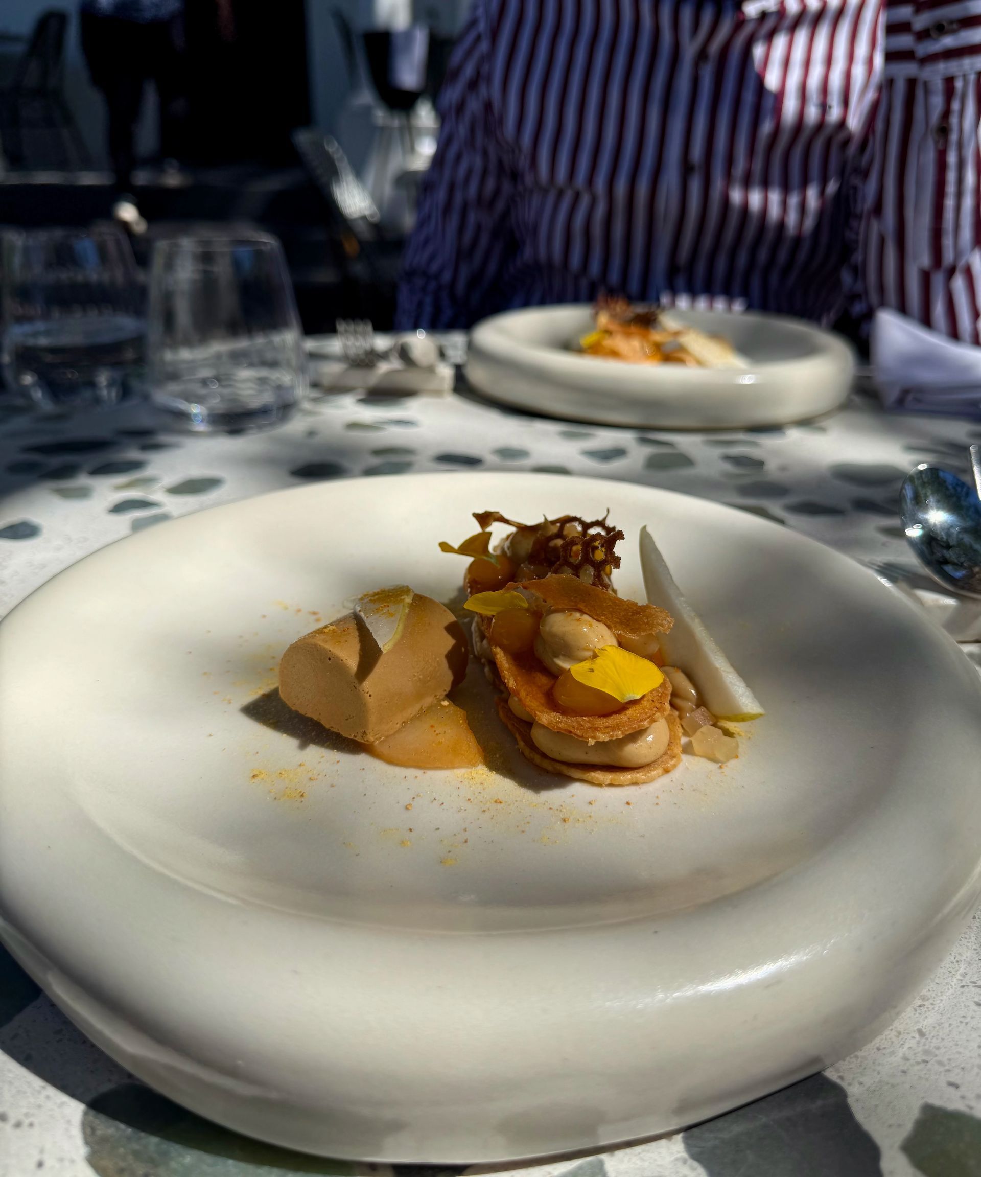 Small plated dish of food with a person in background, dining outside.