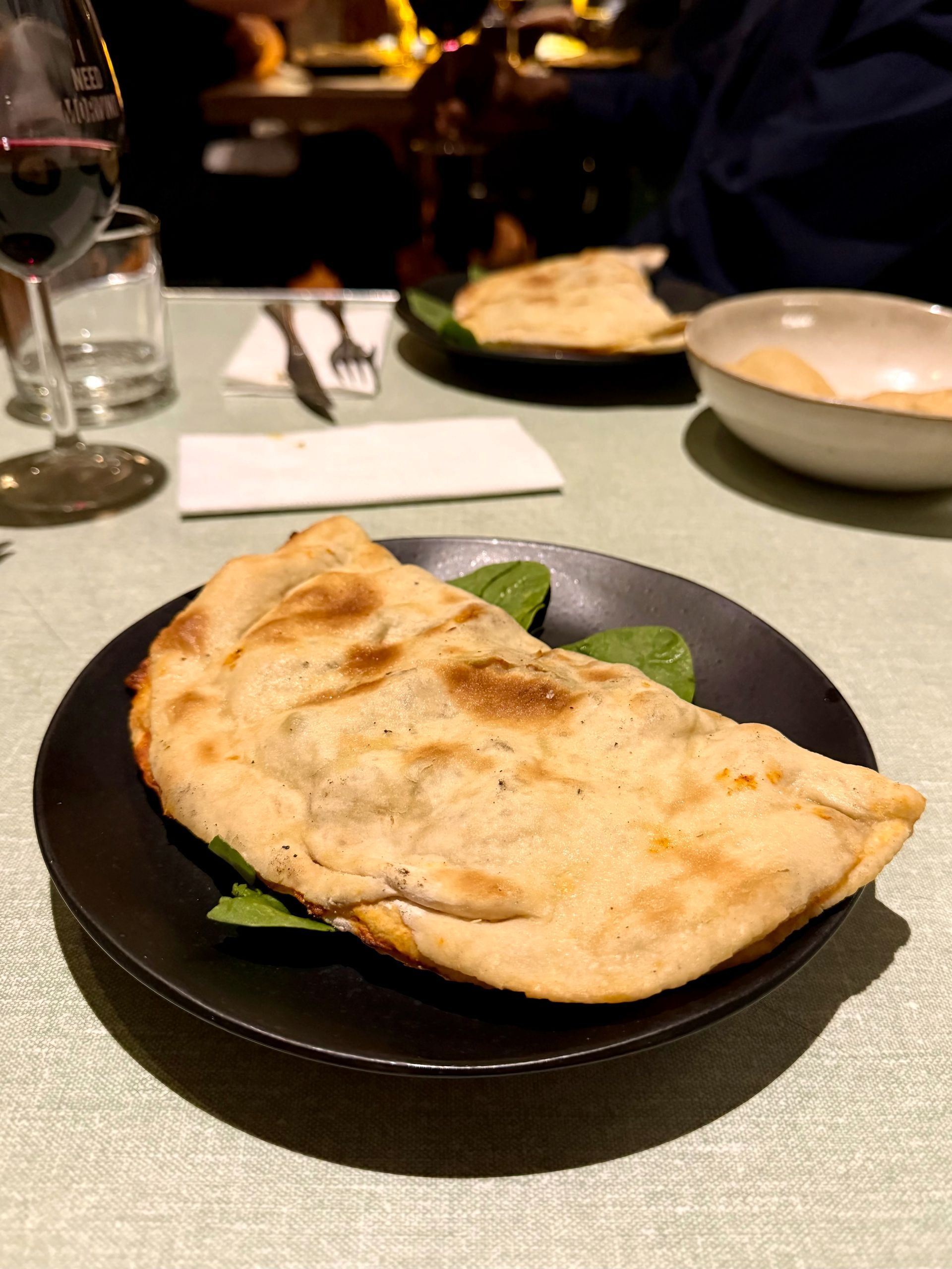 Calzone on black plate with spinach, dining table setting.