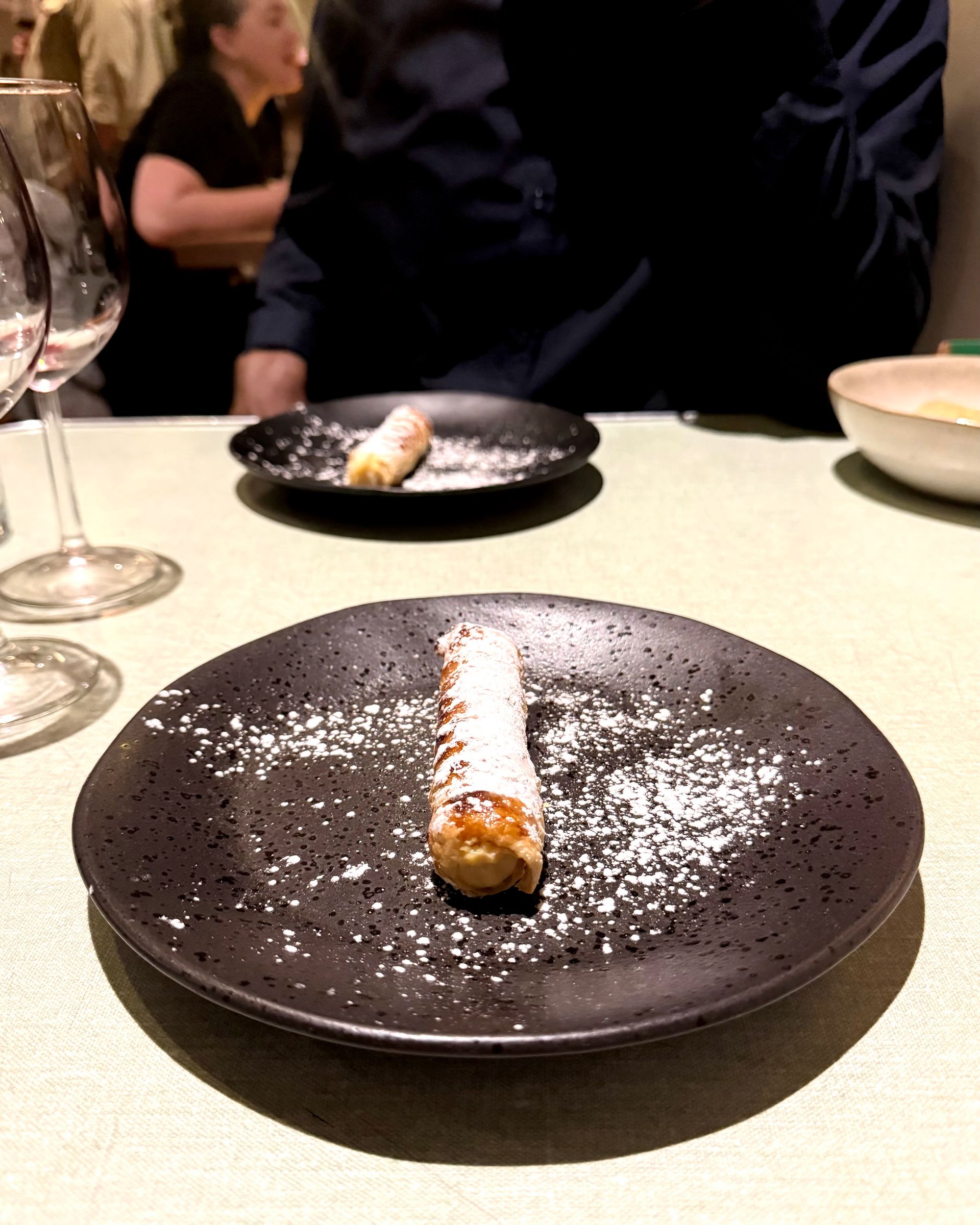 Cannoli on a black plate dusted with powdered sugar, set on a green tablecloth.