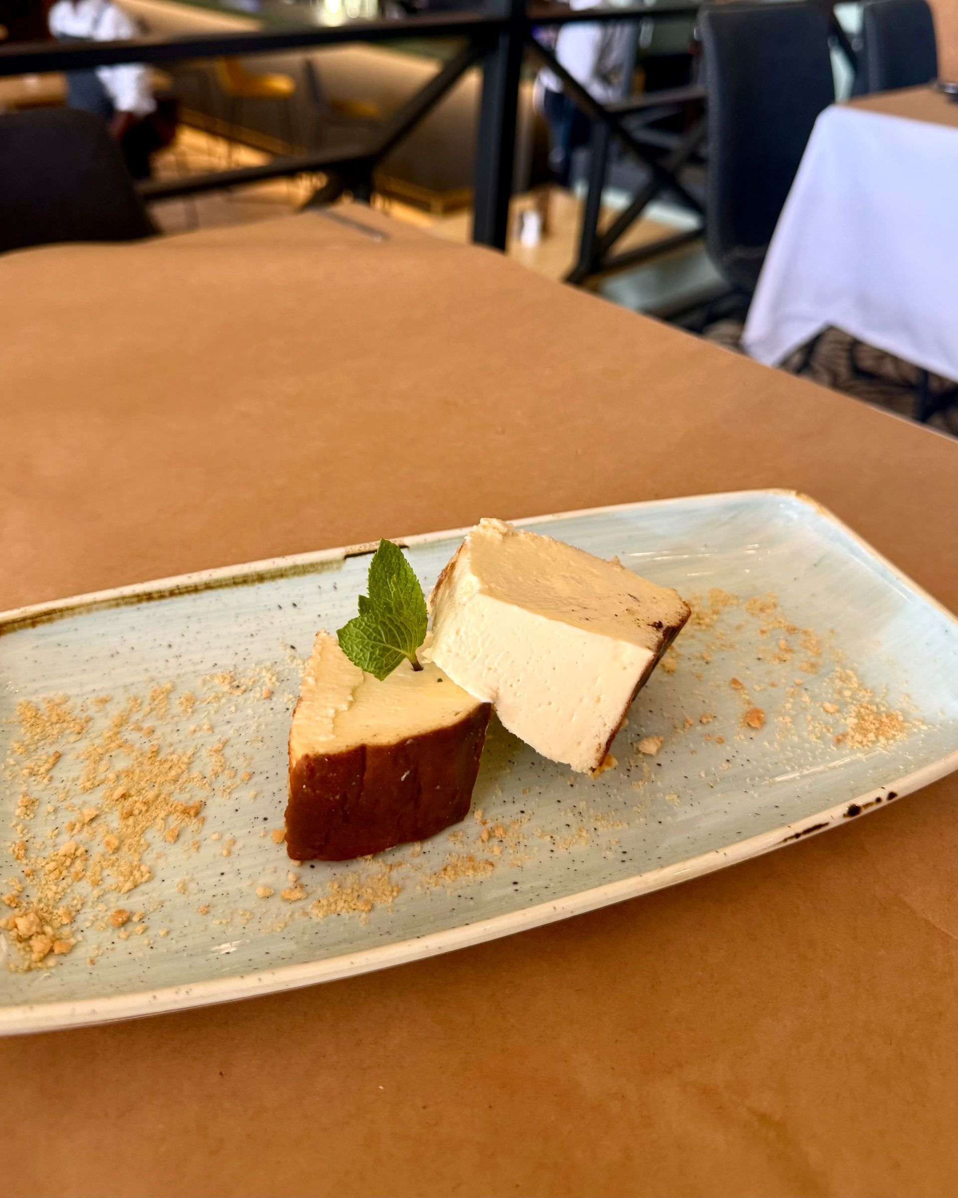 Two slices of dessert on a rectangular plate, garnished with mint and crumbs. Indoor restaurant setting.