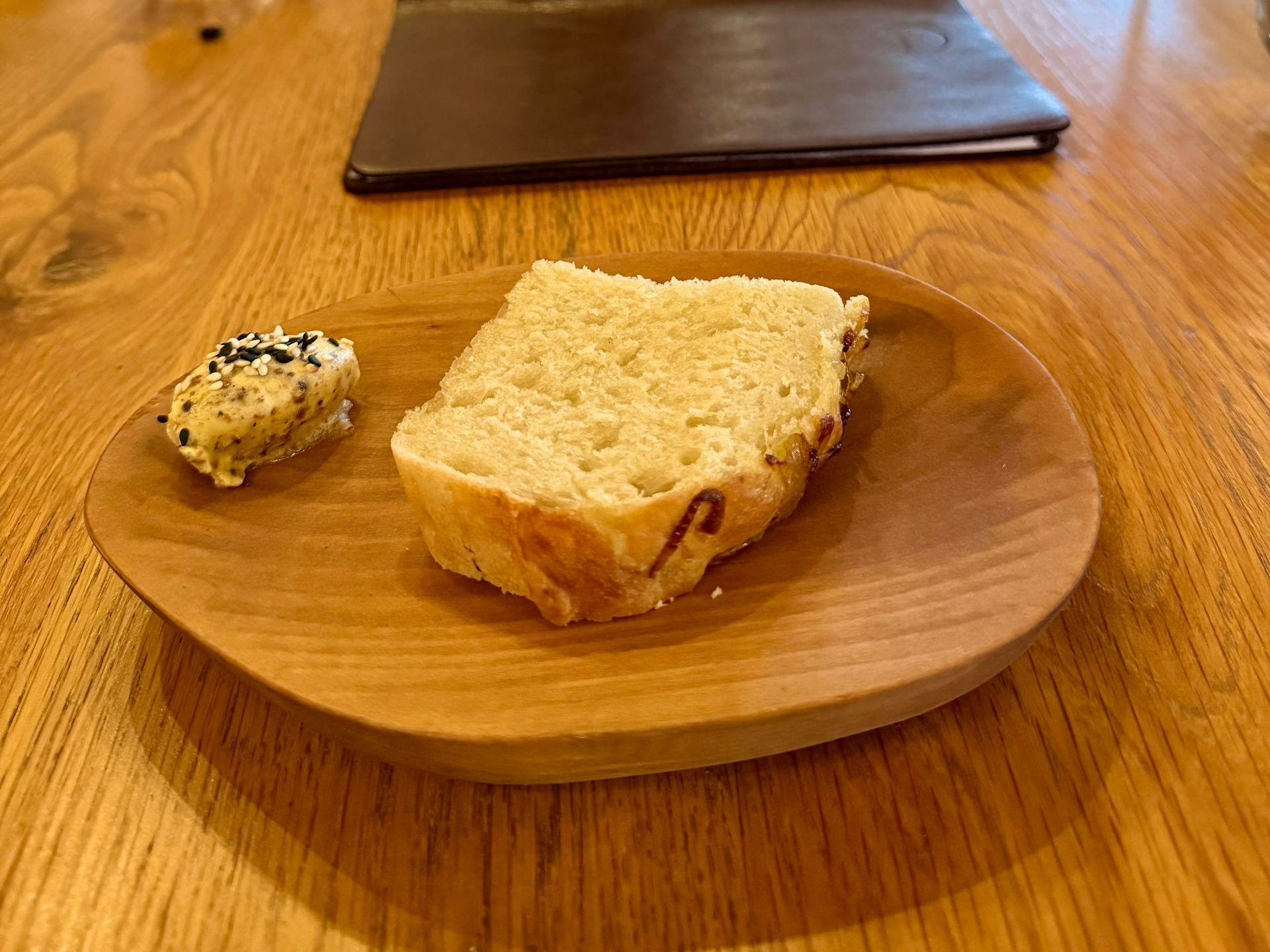 Bread slice and butter on a wooden plate on a wooden table, with a menu in the background.