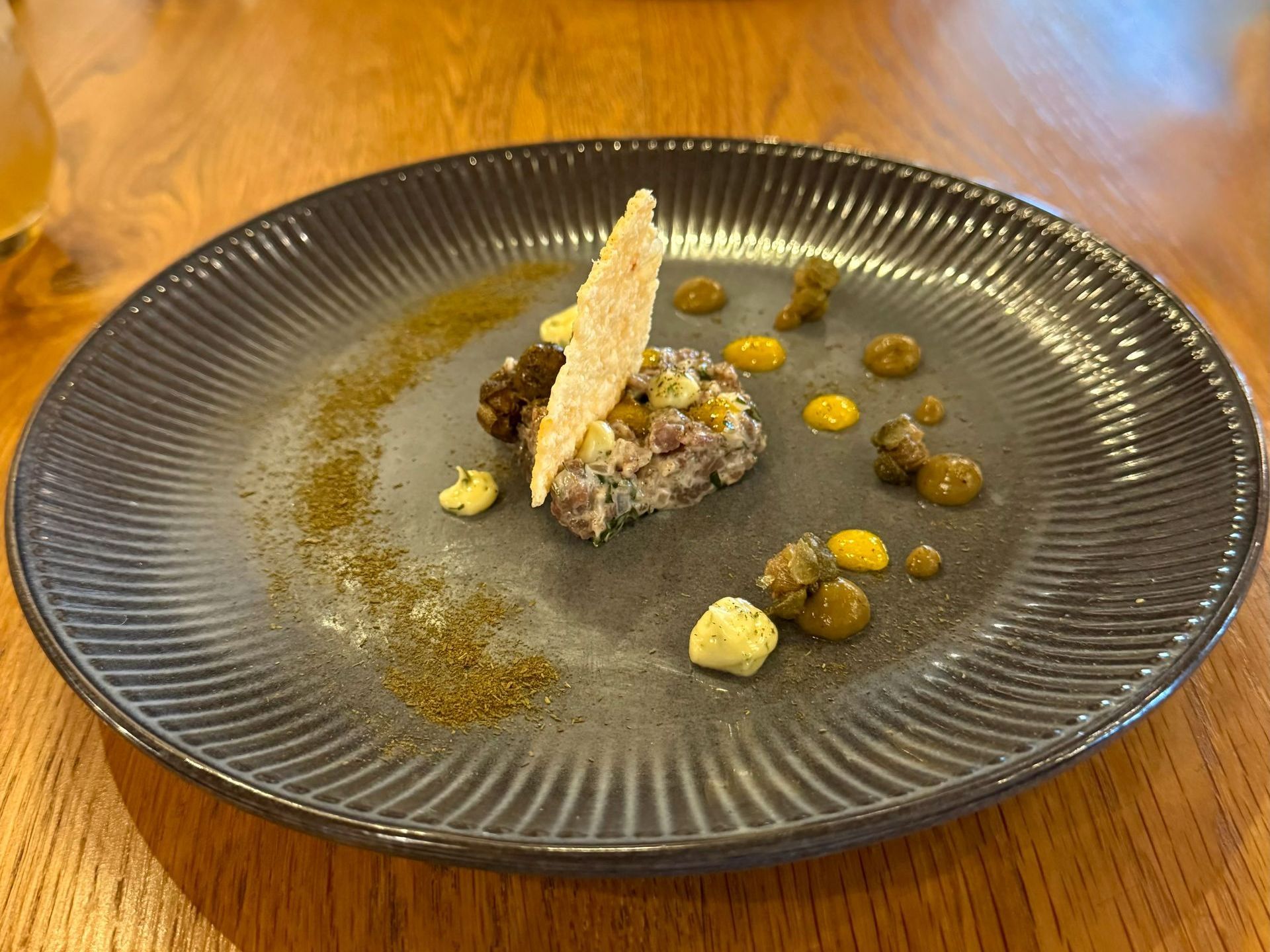 Plate of food, composed of meat, sauces, and crisp cracker, in a restaurant setting.