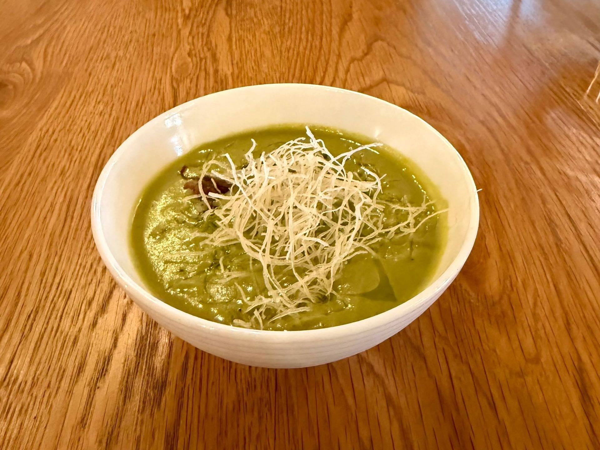 Bowl of green soup with white garnish on a wooden table.