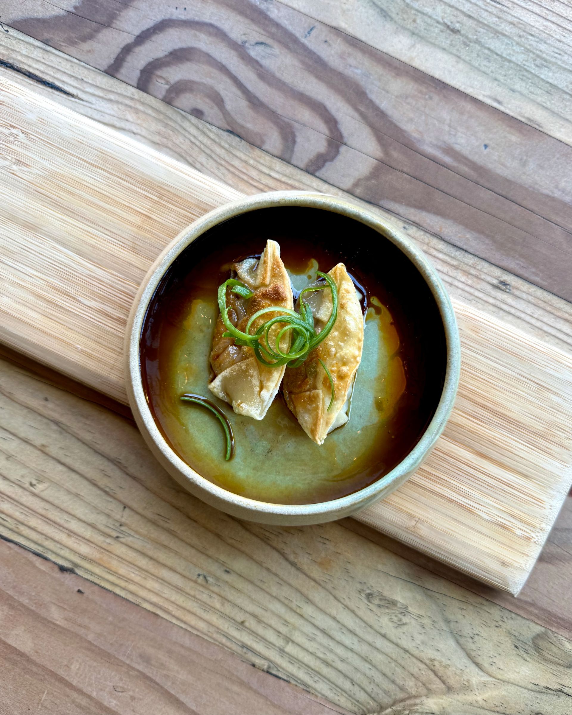 Two fried dumplings in a ceramic bowl, garnished with green onion, on a wooden board.