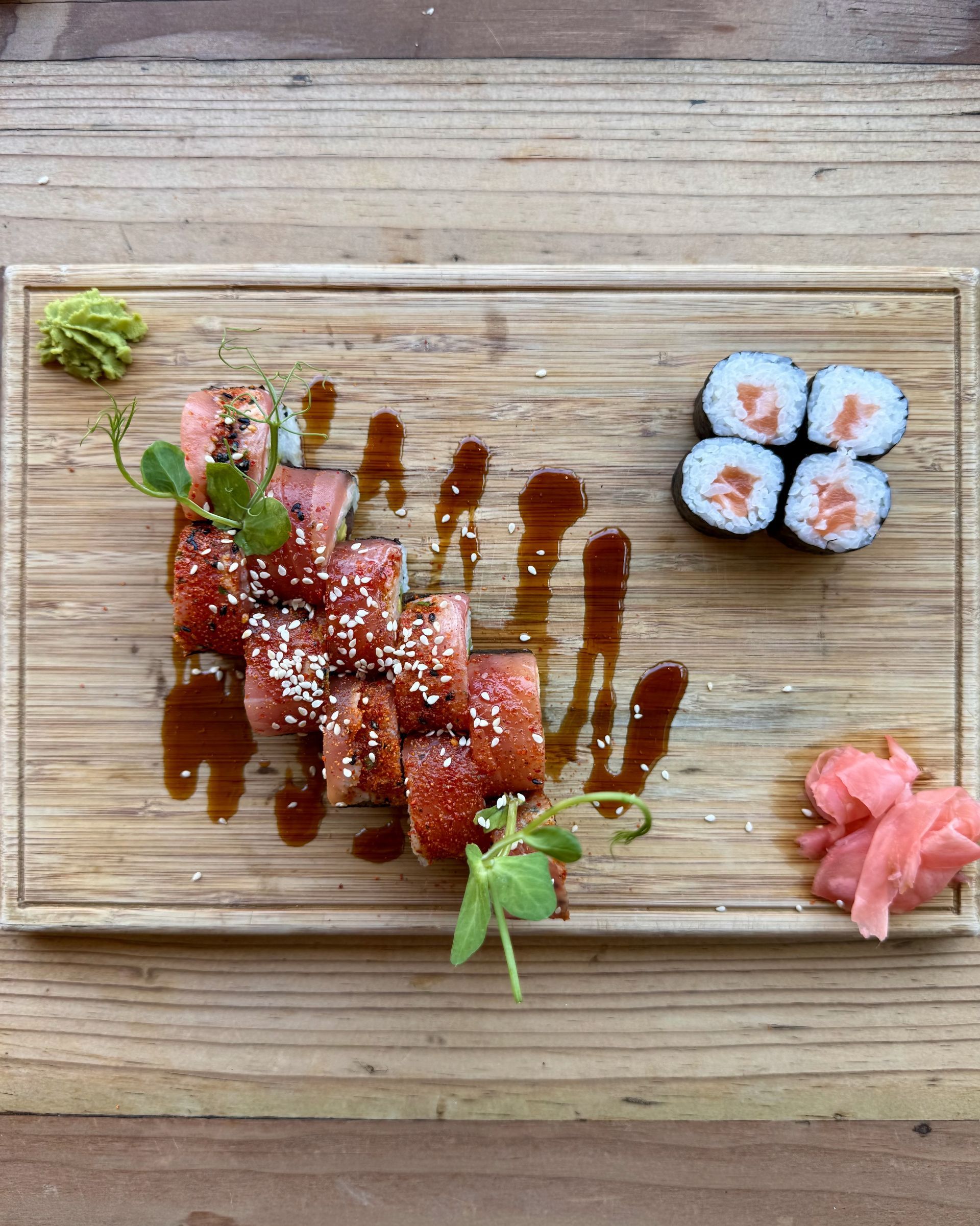 Sushi platter with rolls, salmon maki, wasabi, ginger, and sauce on a wooden board.