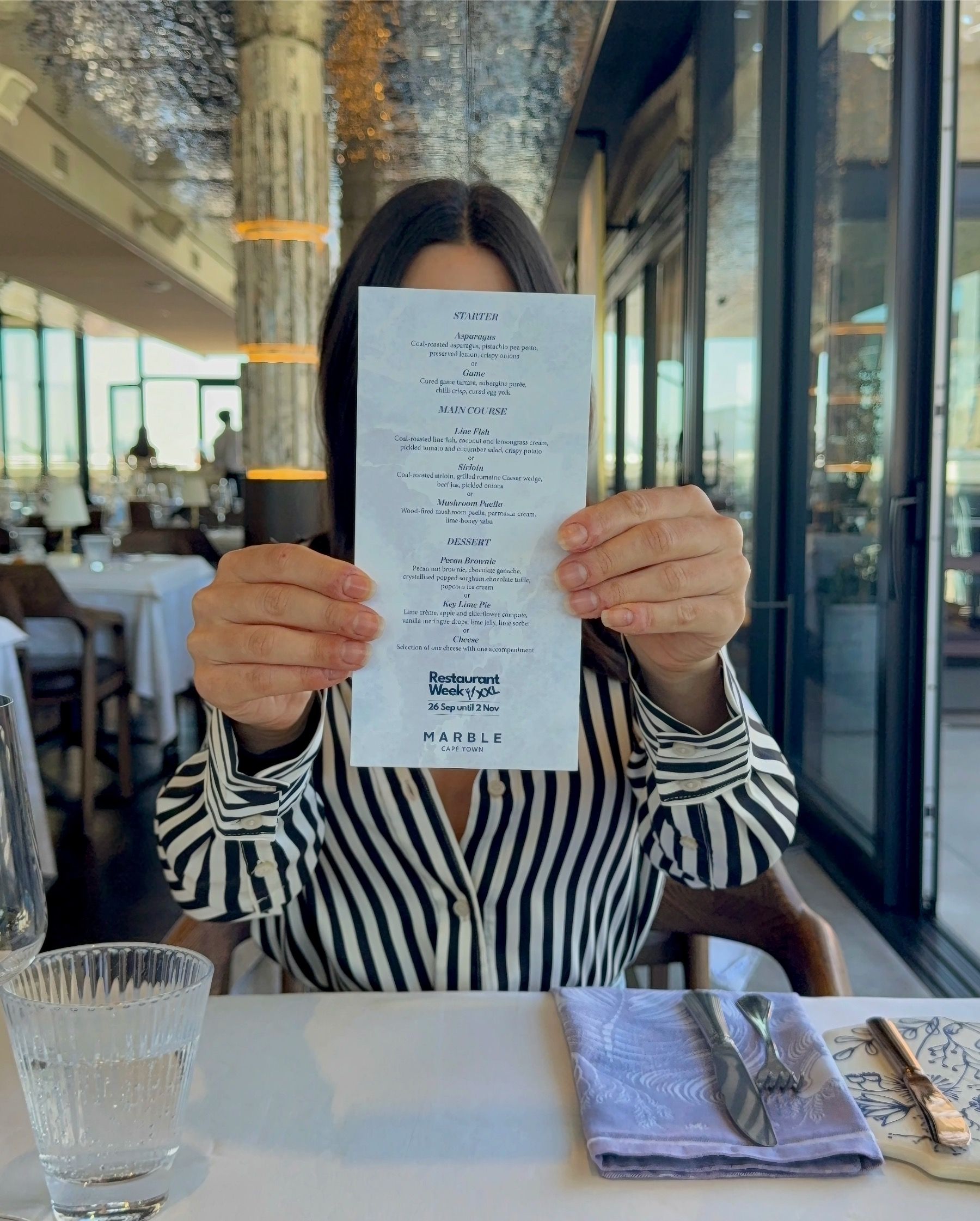 Paige holding the Marble Cape Town Restaurant Week menu inside the V&A Waterfront dining room.