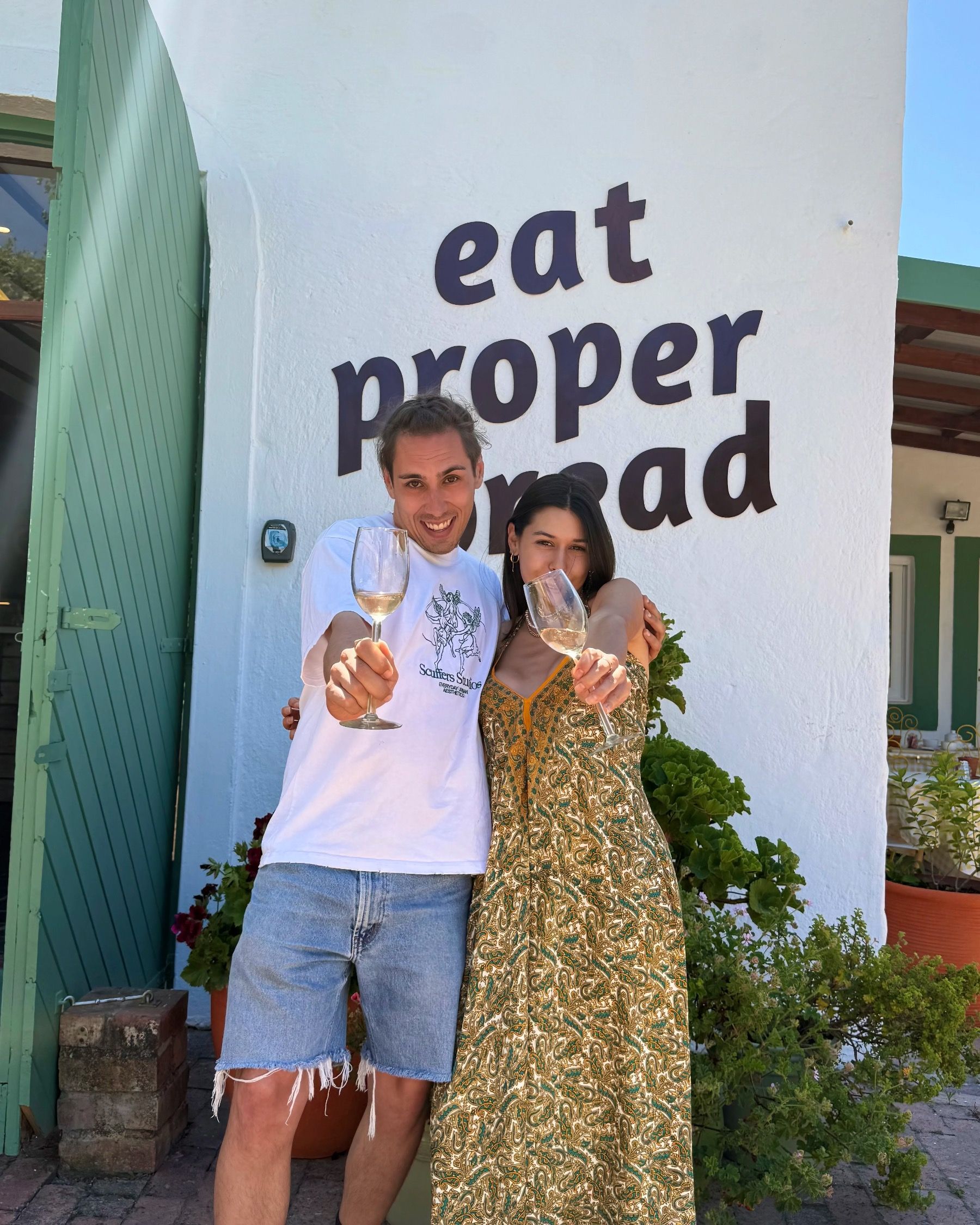 Paige celebrating the Motherdough Jonkershoek opening with sparkling wine in front of the bakery’s “Eat Proper Bread” wall